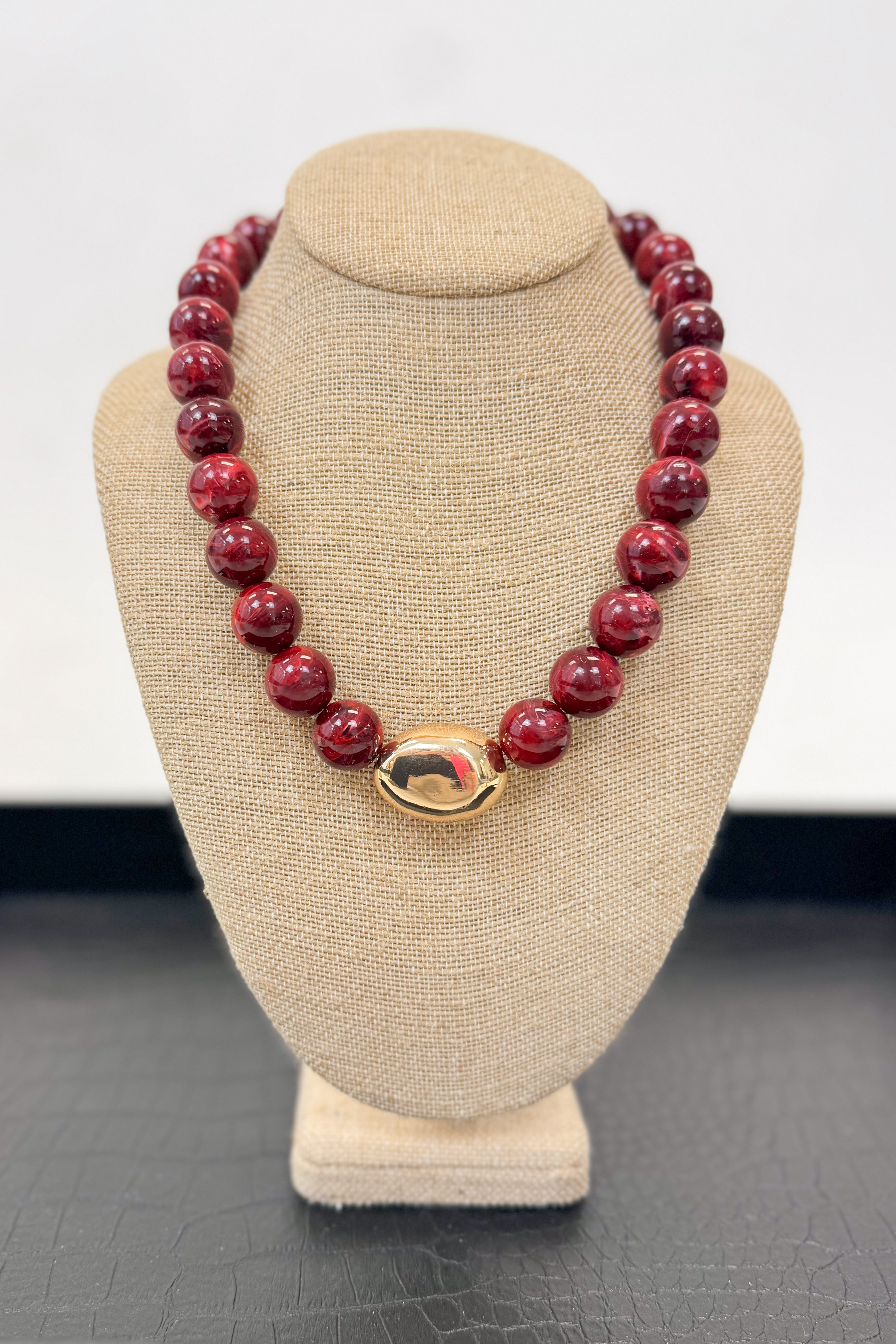 Wine colored beaded necklace with a gold clasp on a gray bust
