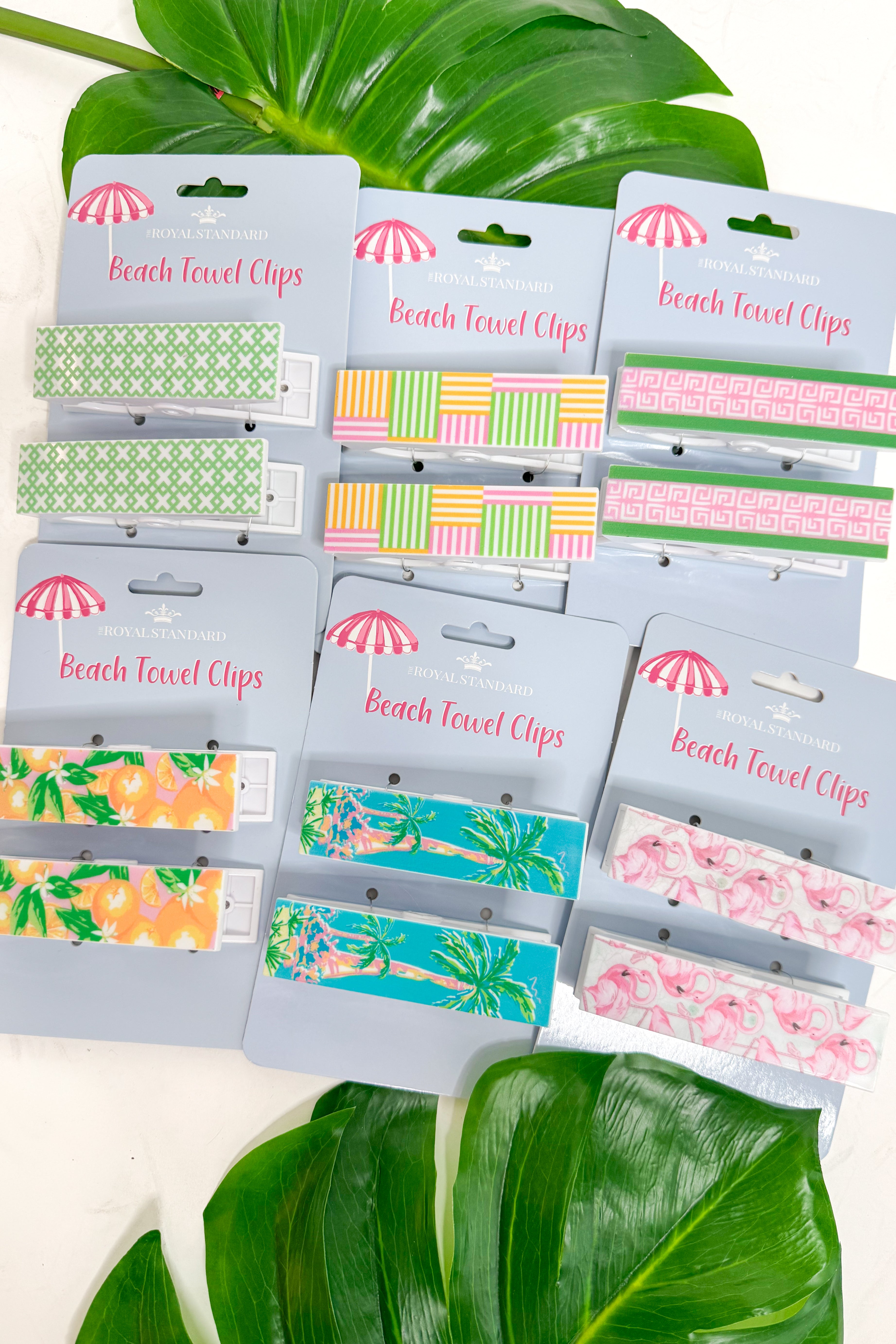 Packaged beach towel clips with colorful designs on a white background with green leaves.