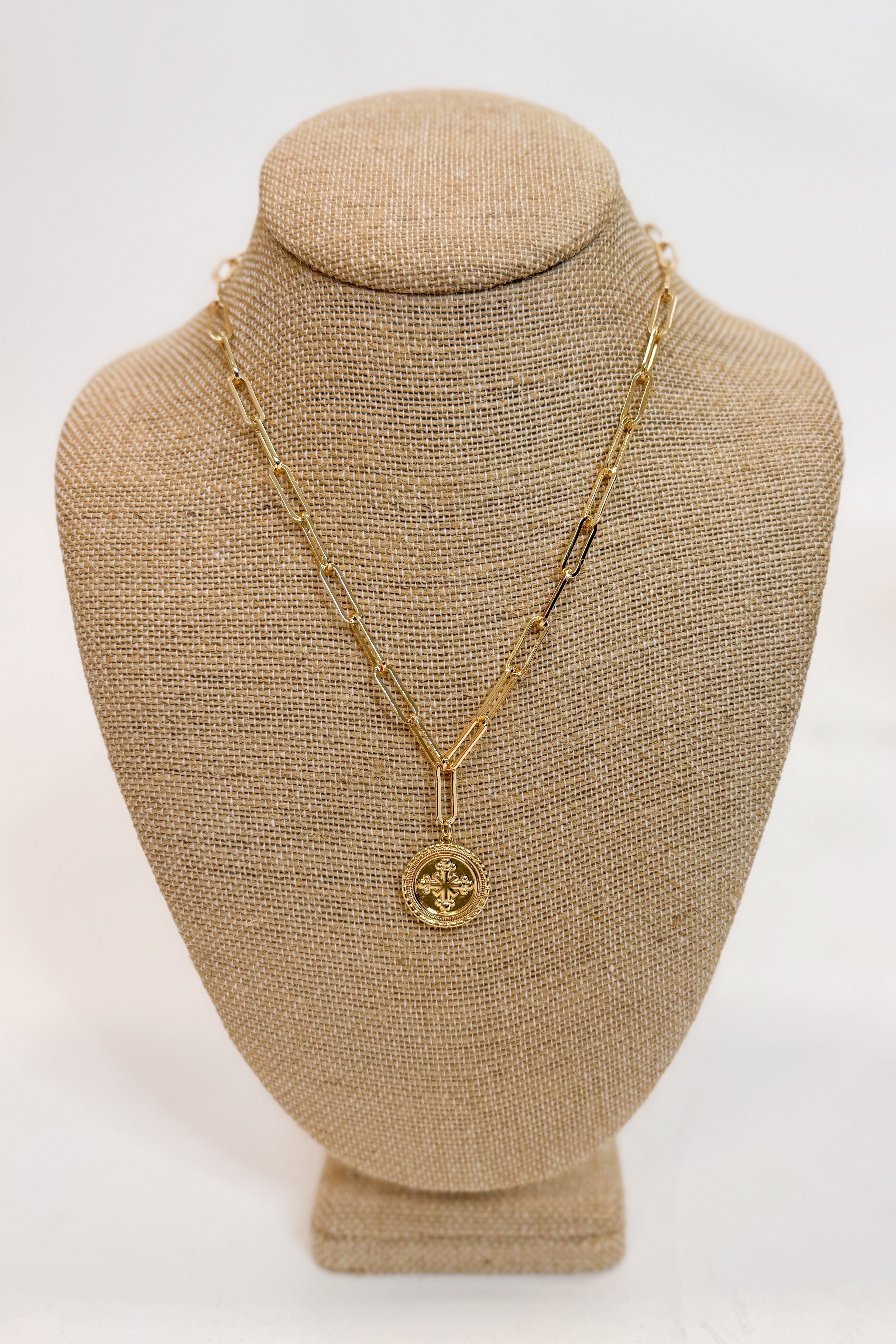 Gold necklace with a pendant on a beige bust against a white background