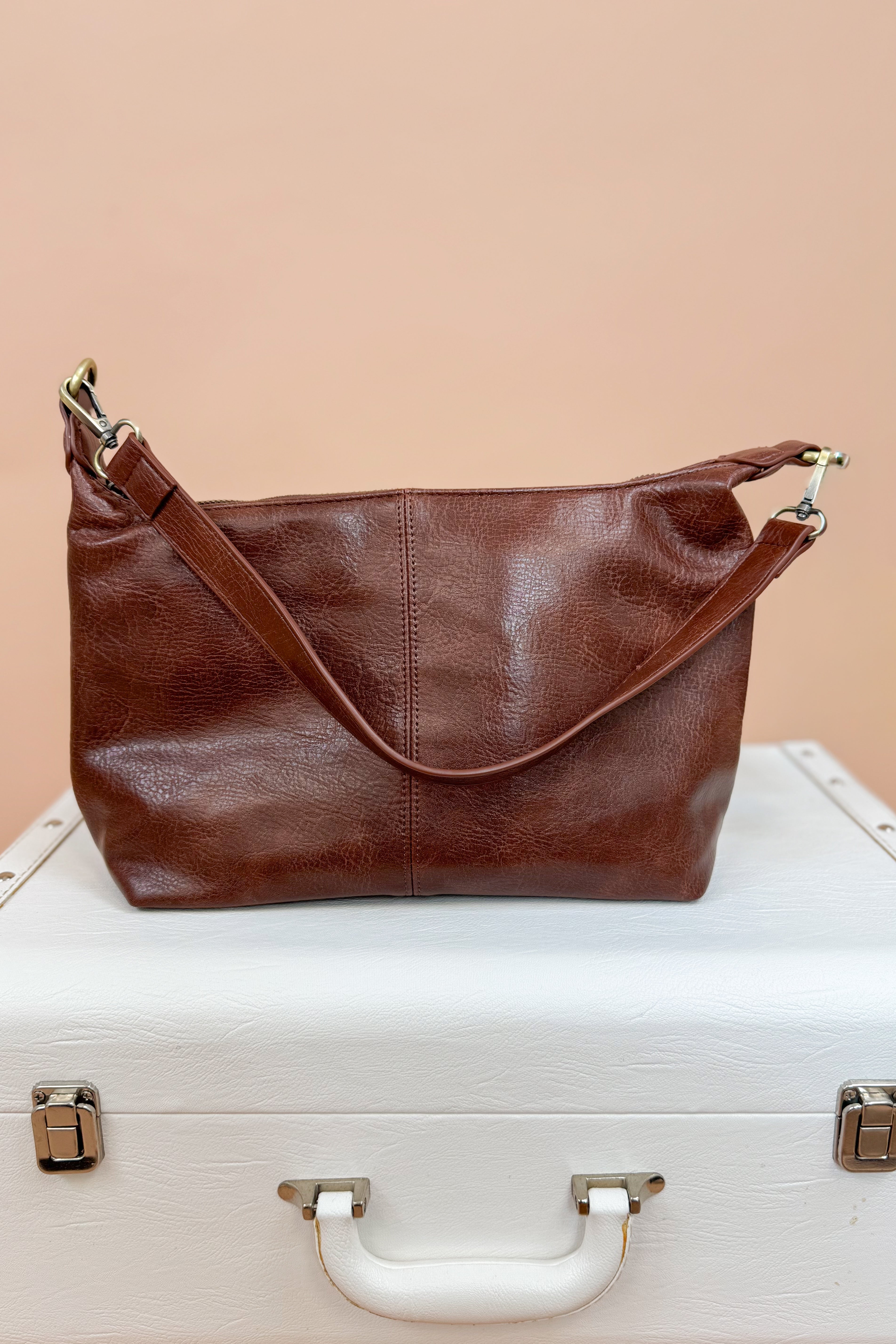Brown leather handbag on a white suitcase with a beige background