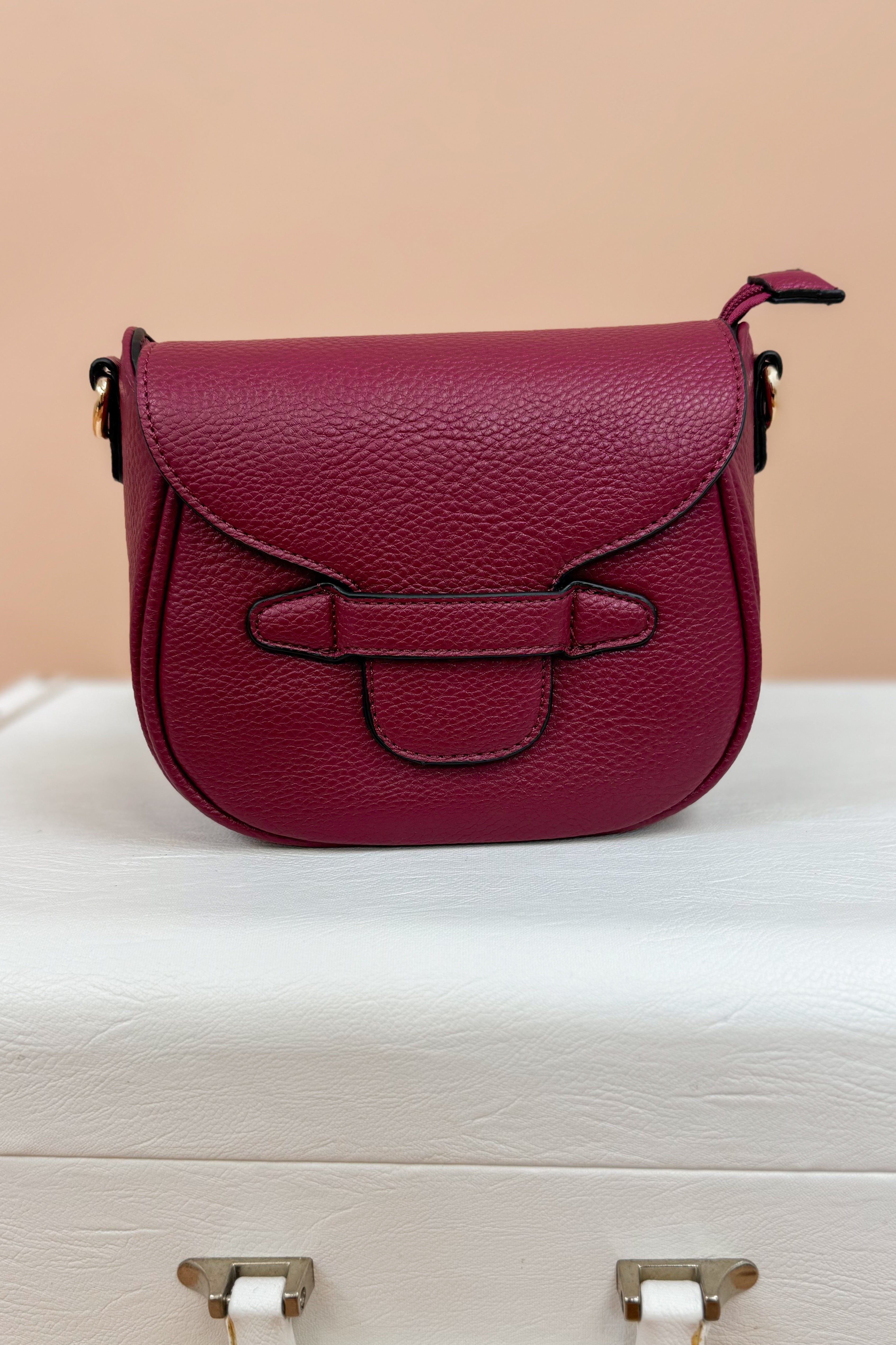 Magenta handbag on a white surface with a beige background