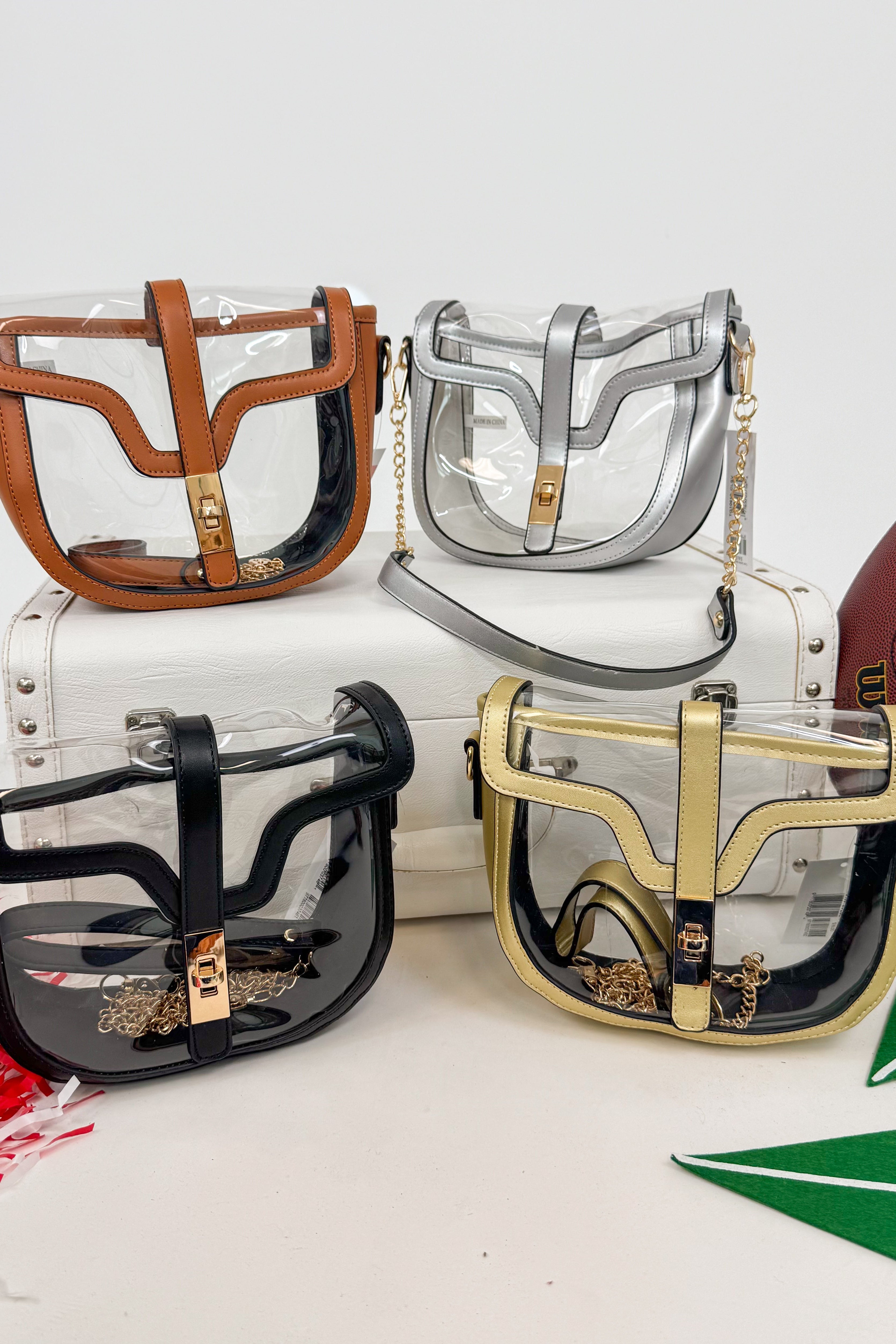 Four transparent handbags in different colors with gold accents on a white surface.
