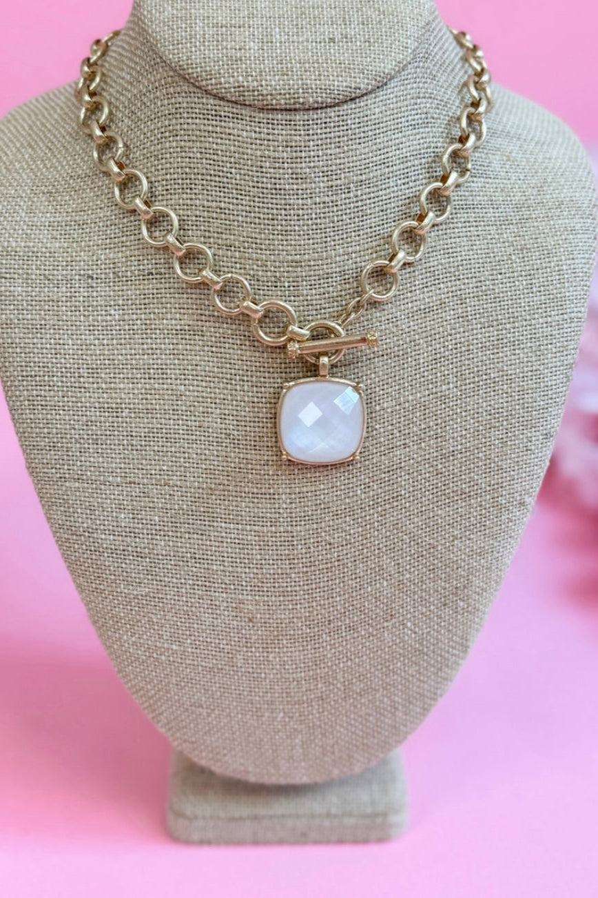 Necklace with a gold chain and white pendant on a mannequin bust against a pink background