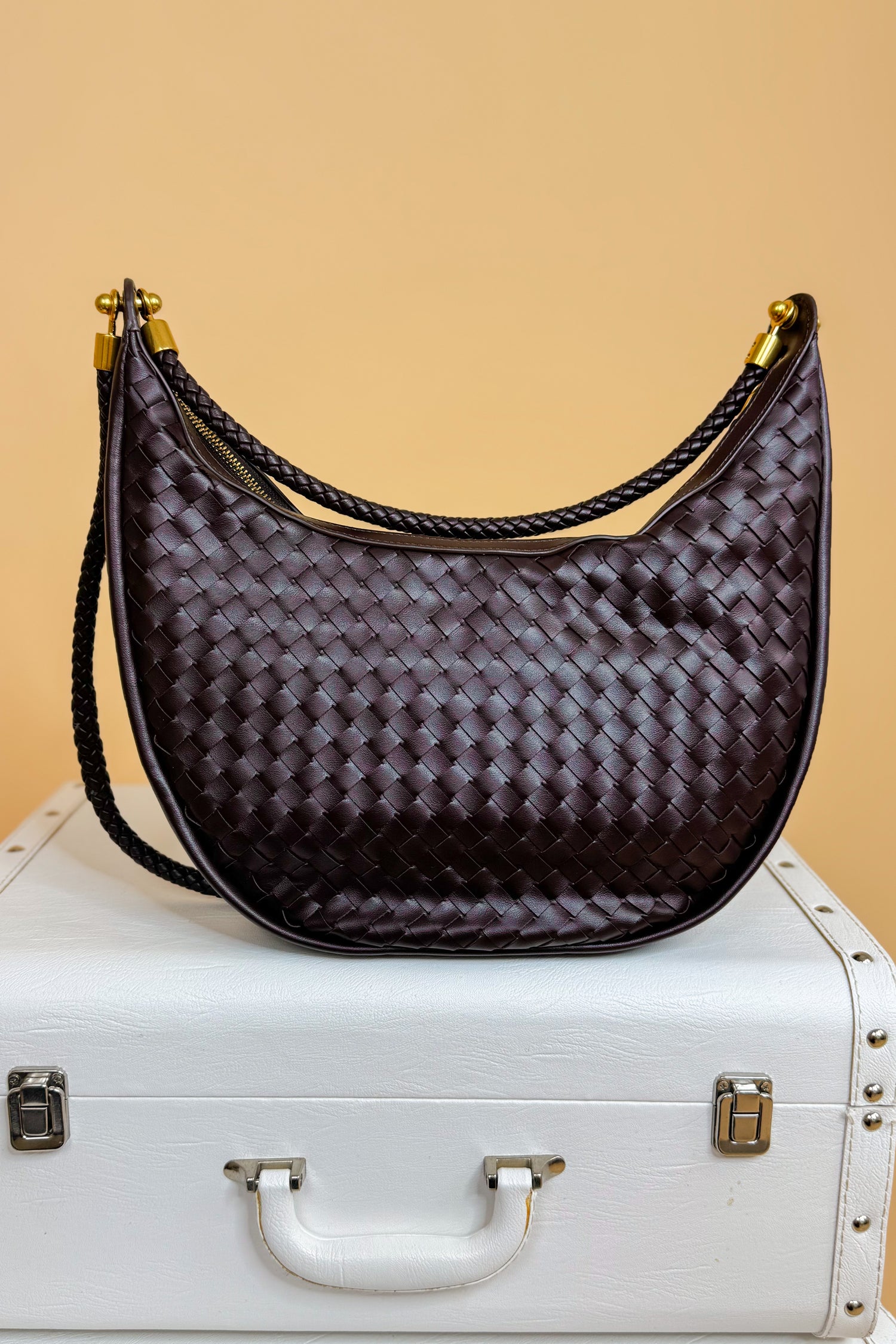 Brown woven handbag on a white suitcase with a beige background