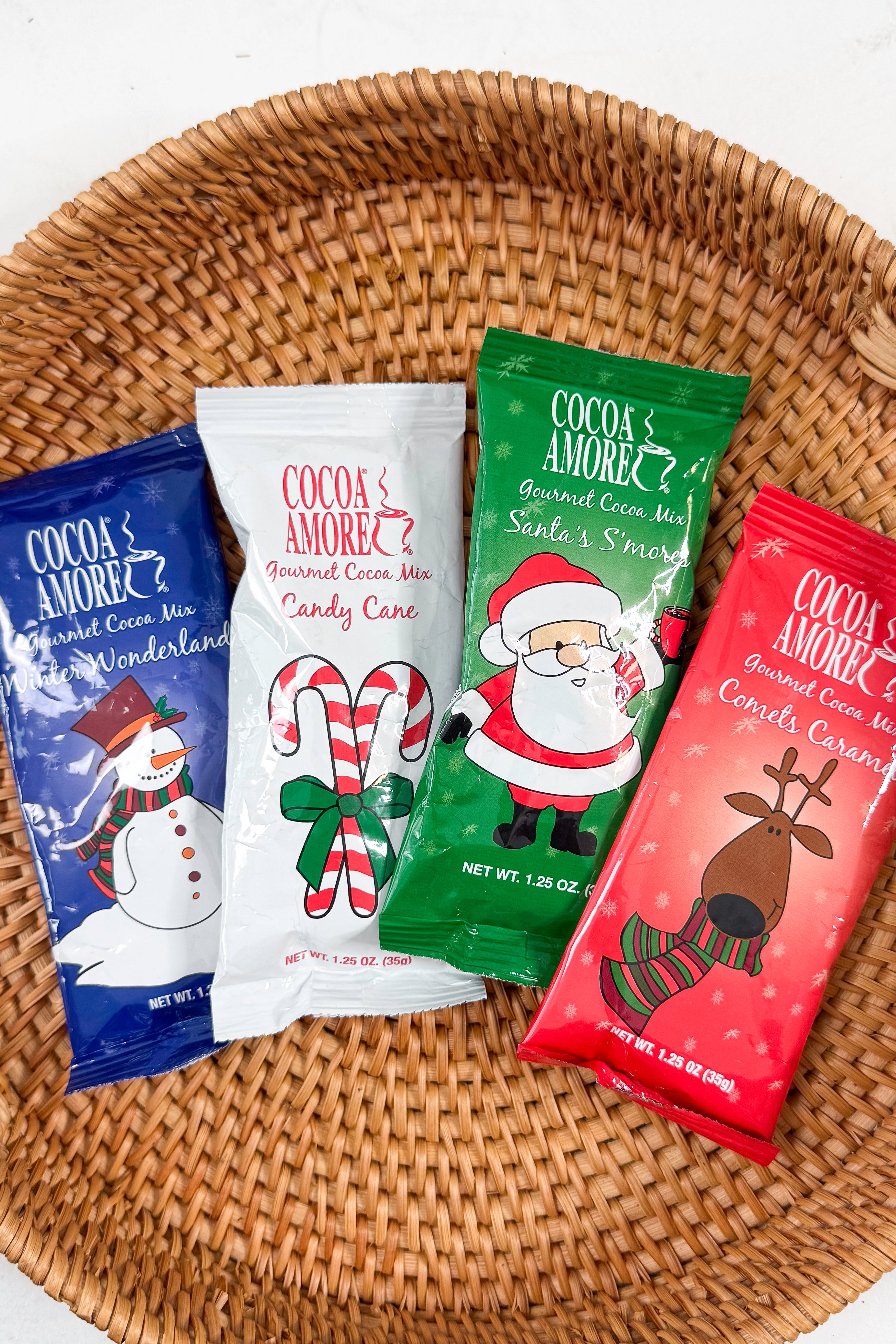 Cocoa Amore Gourmet Cocoa Mix packages with illustrations on a patterned background.