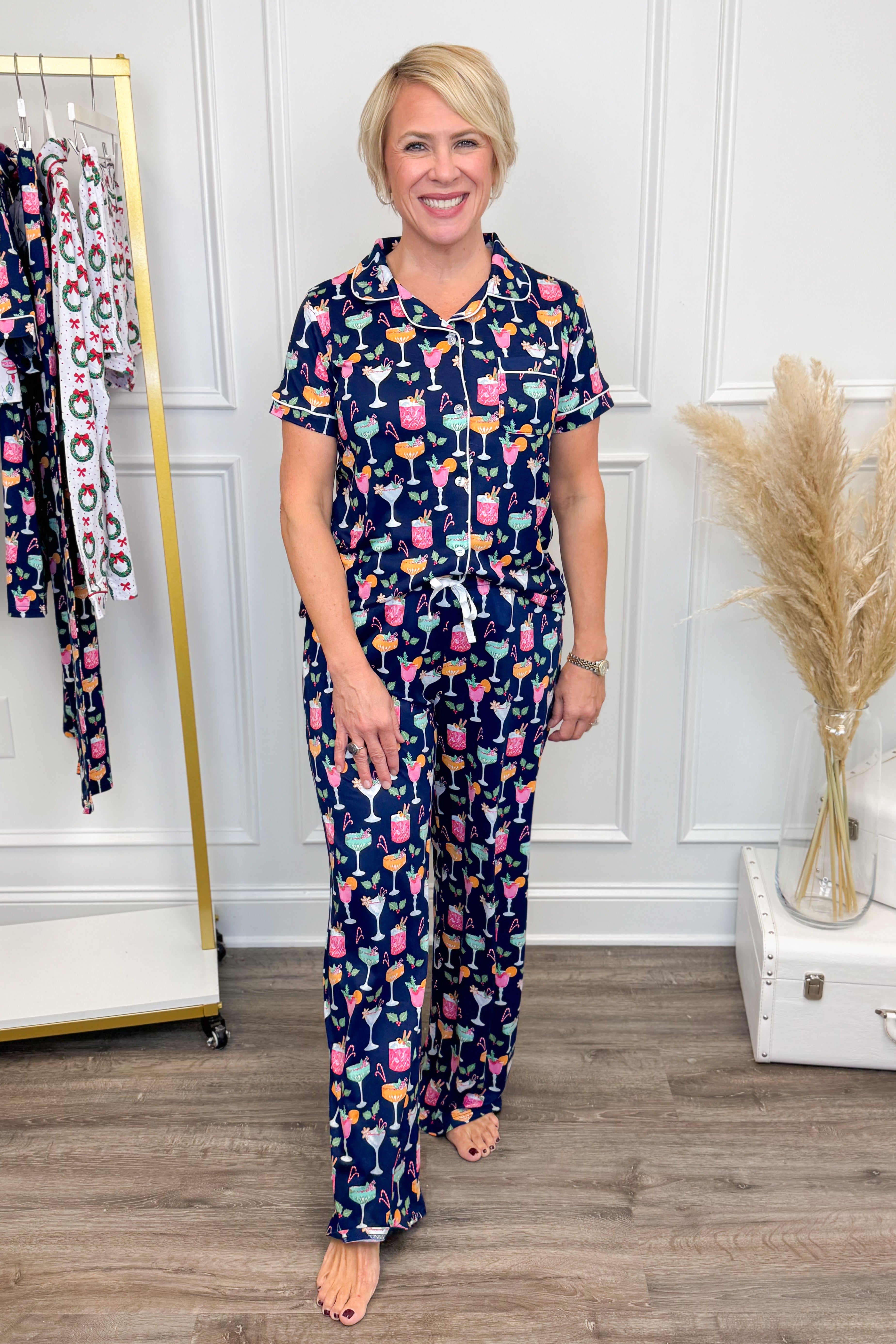 Woman wearing a navy pajama set with colorful pattern in a room with a clothing rack and decorative elements.