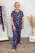 Woman wearing a navy pajama set with colorful pattern in a room with a clothing rack and decorative elements.