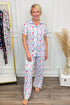 Woman wearing a patterned pajama set in a room with a white wall and wooden floor.