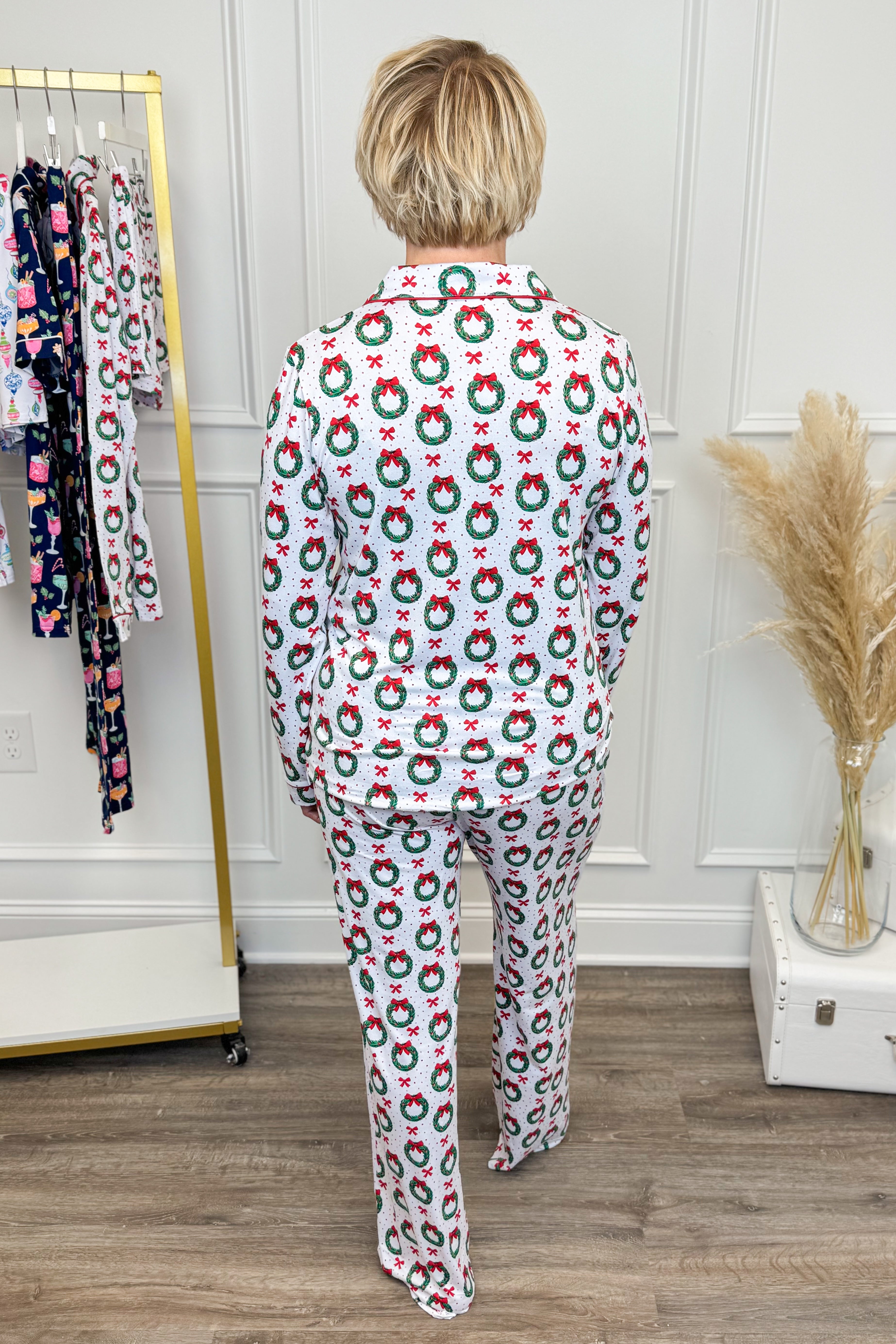 Person wearing a festive pajama set with wreath pattern in a room setting.