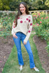 Woman wearing a floral sweater and blue jeans standing in a garden.