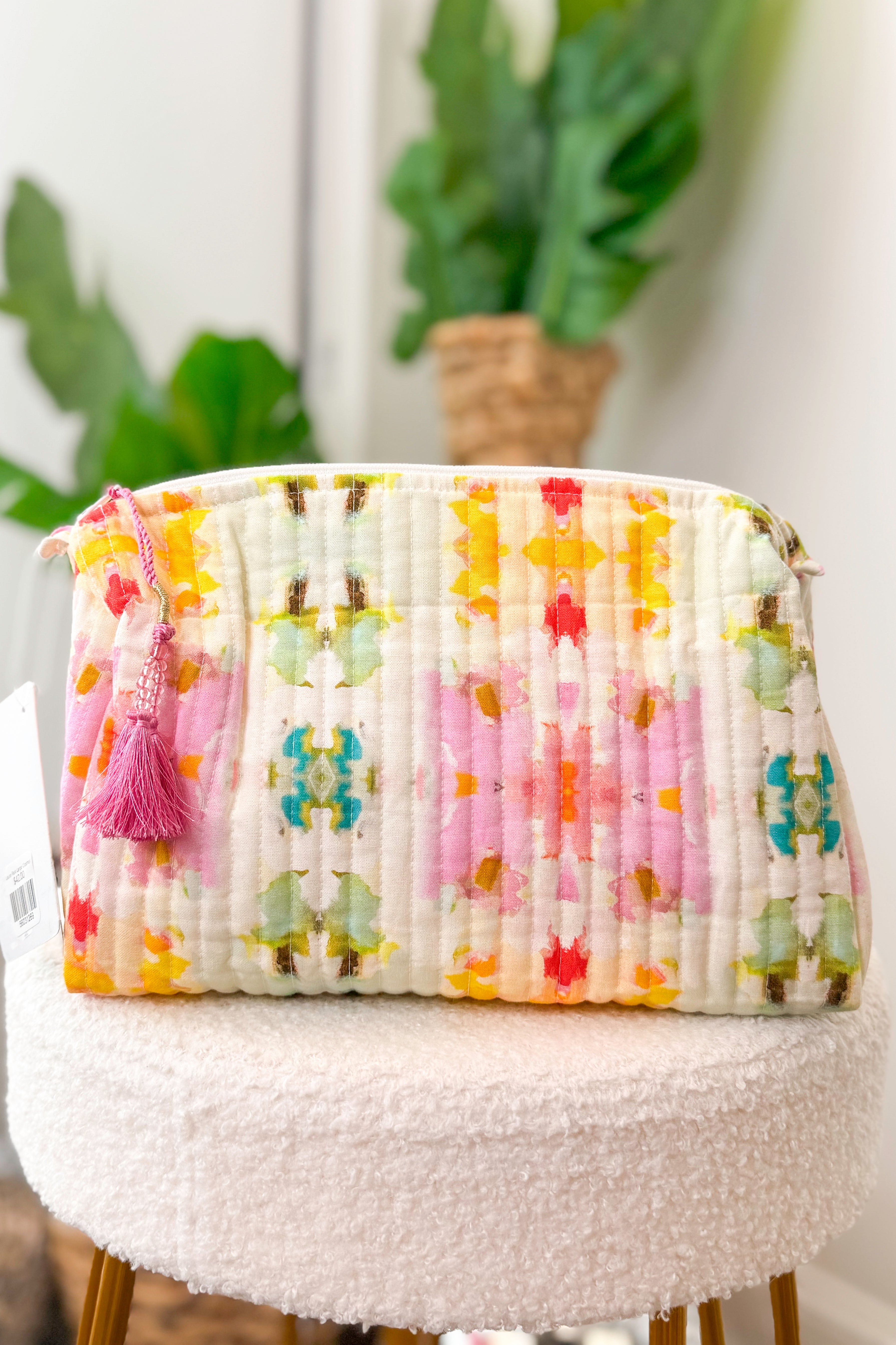 Floral-patterned bag with tassel on a white surface with plants in the background
