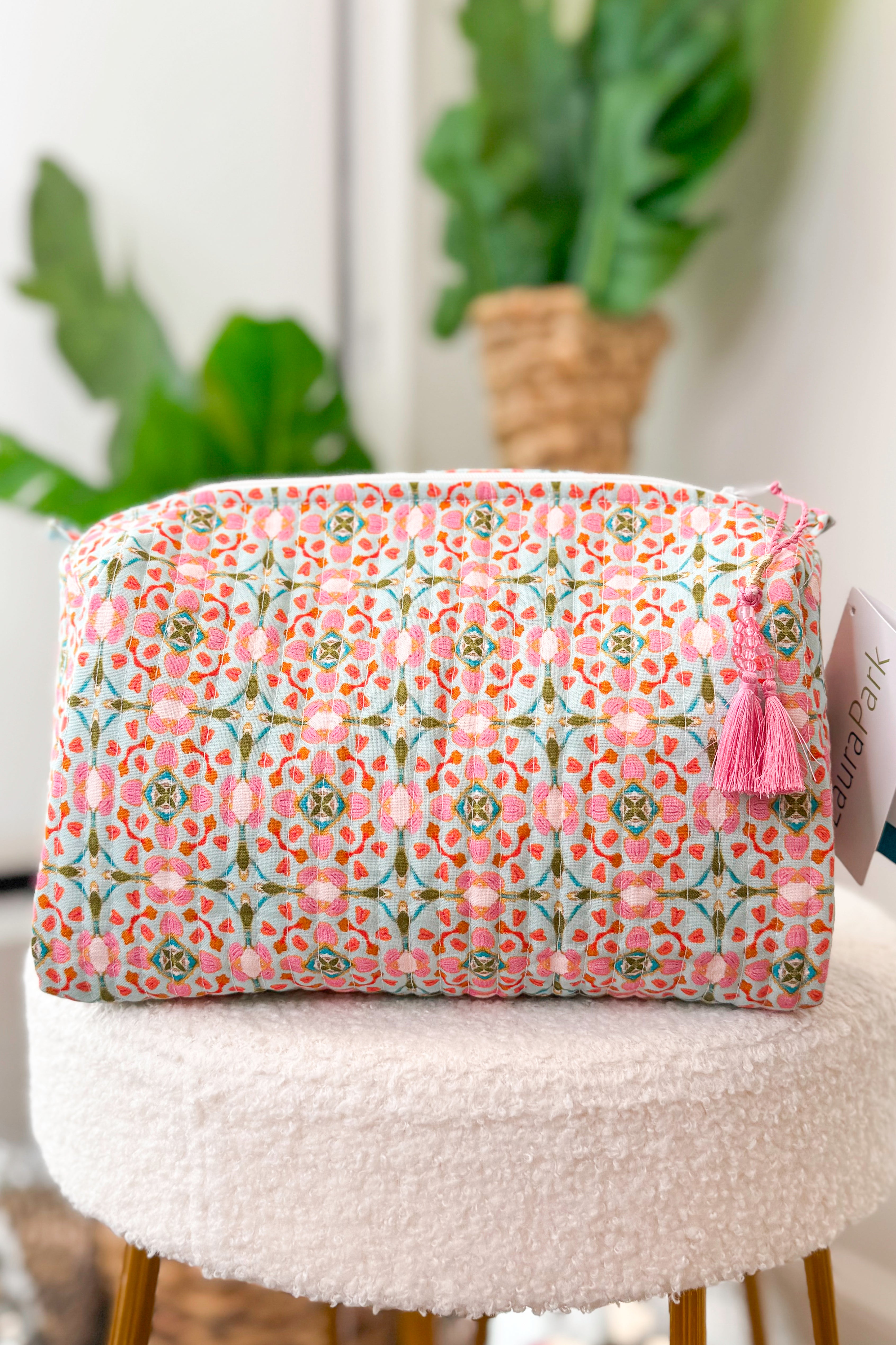 Floral patterned pouch with a pink tassel on a white surface with plants in the background