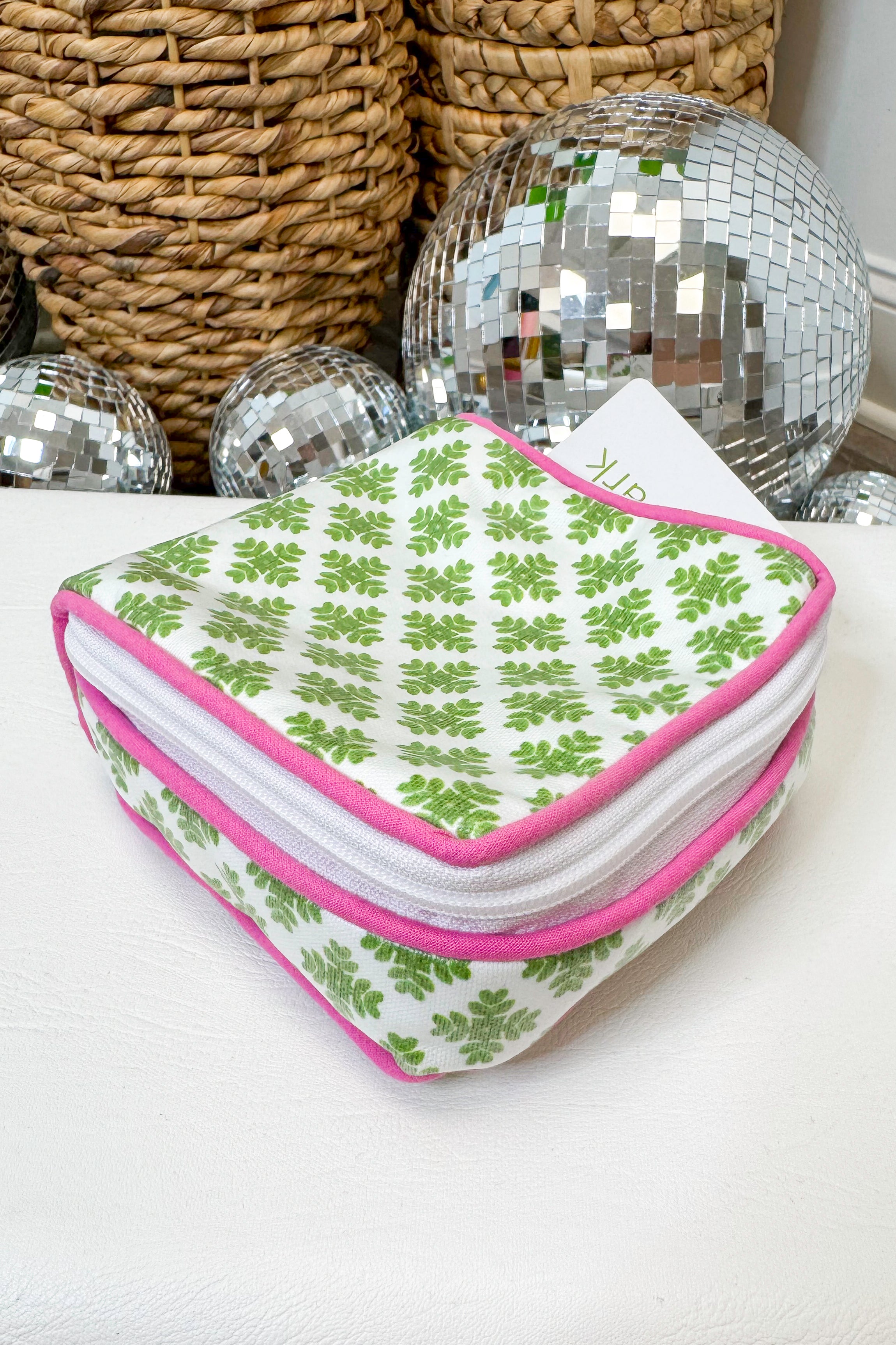 Heart-shaped pouch with green floral pattern and pink border on a white surface with disco balls in the background.