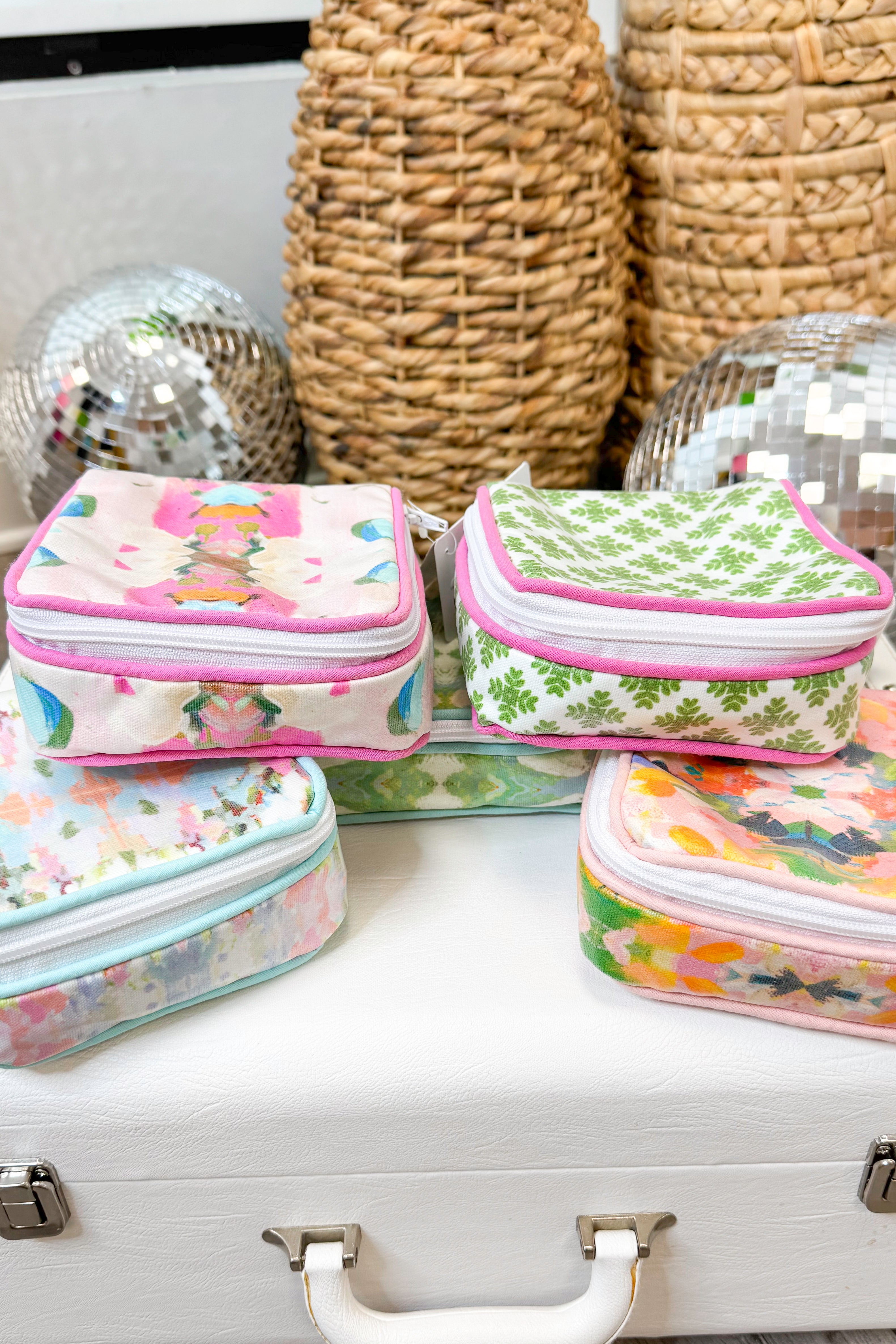 Set of floral-patterned makeup bags on a white surface with decorative items in the background.