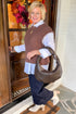 Woman wearing brown sweater and white shirt with jeans at a front door.
