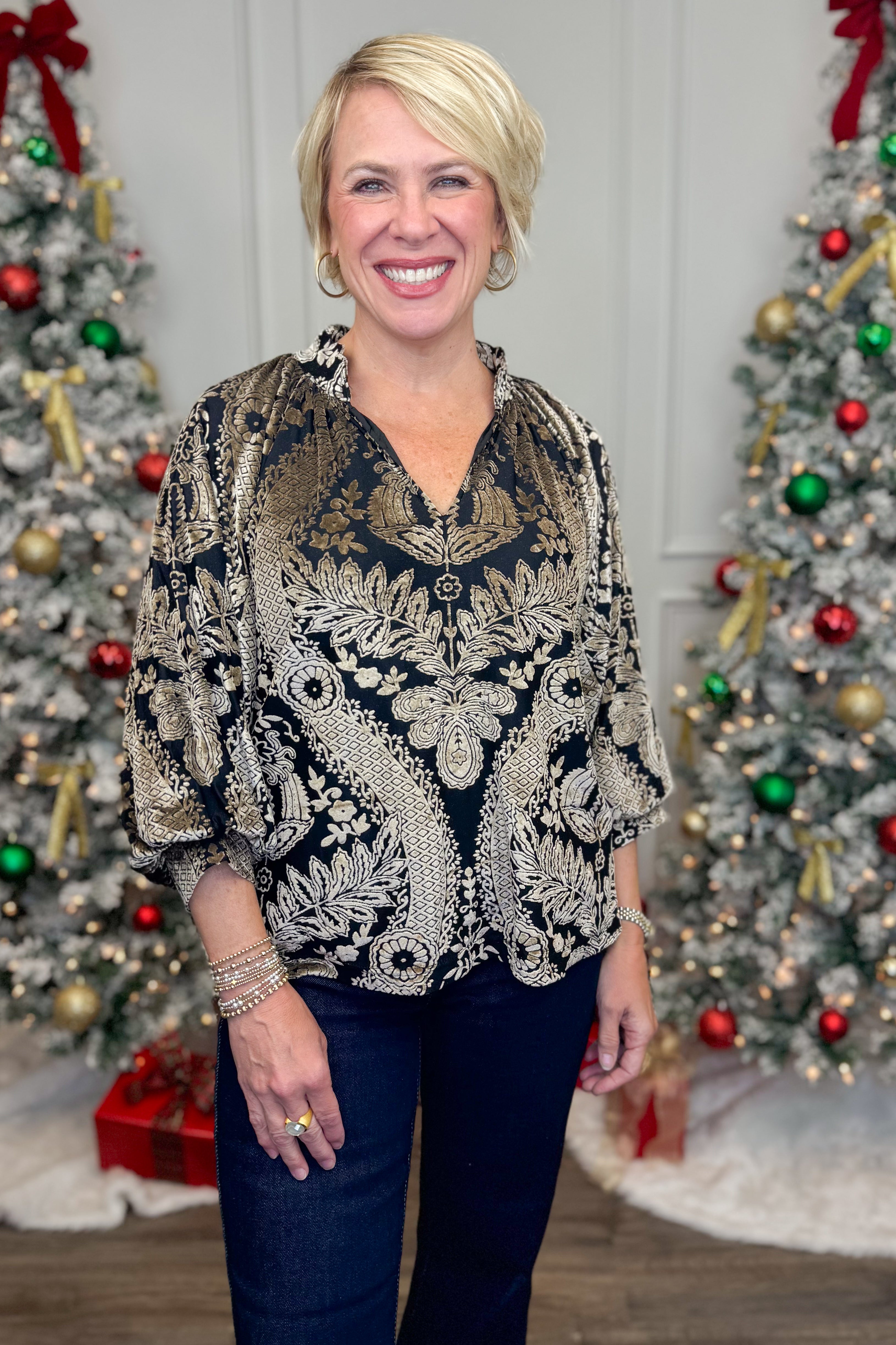 Front view of woman wearing Black With Velvet Pattern Top with jeans with holiday decor in the background.