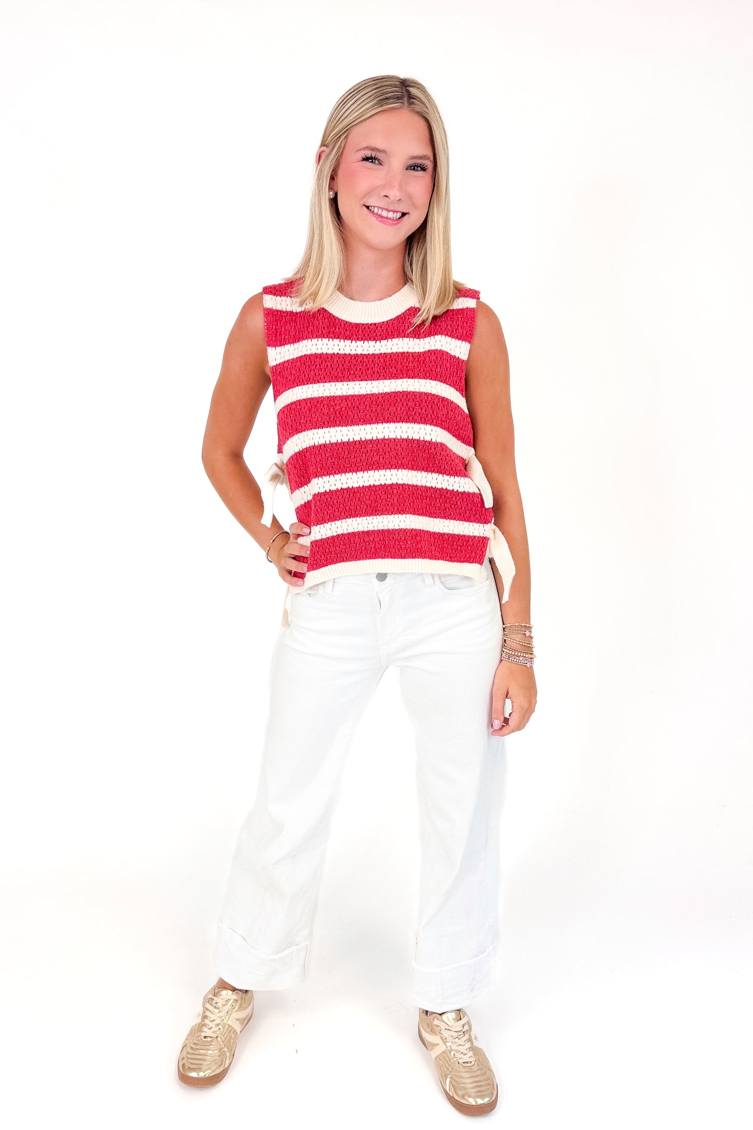 Woman wearing a red and white striped sleeveless top with white pants on a white background
