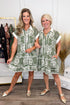 Two women wearing matching green and white patterned dresses standing in a room with clothing racks.