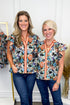 Two women wearing floral tops with zipper details in a clothing store setting.