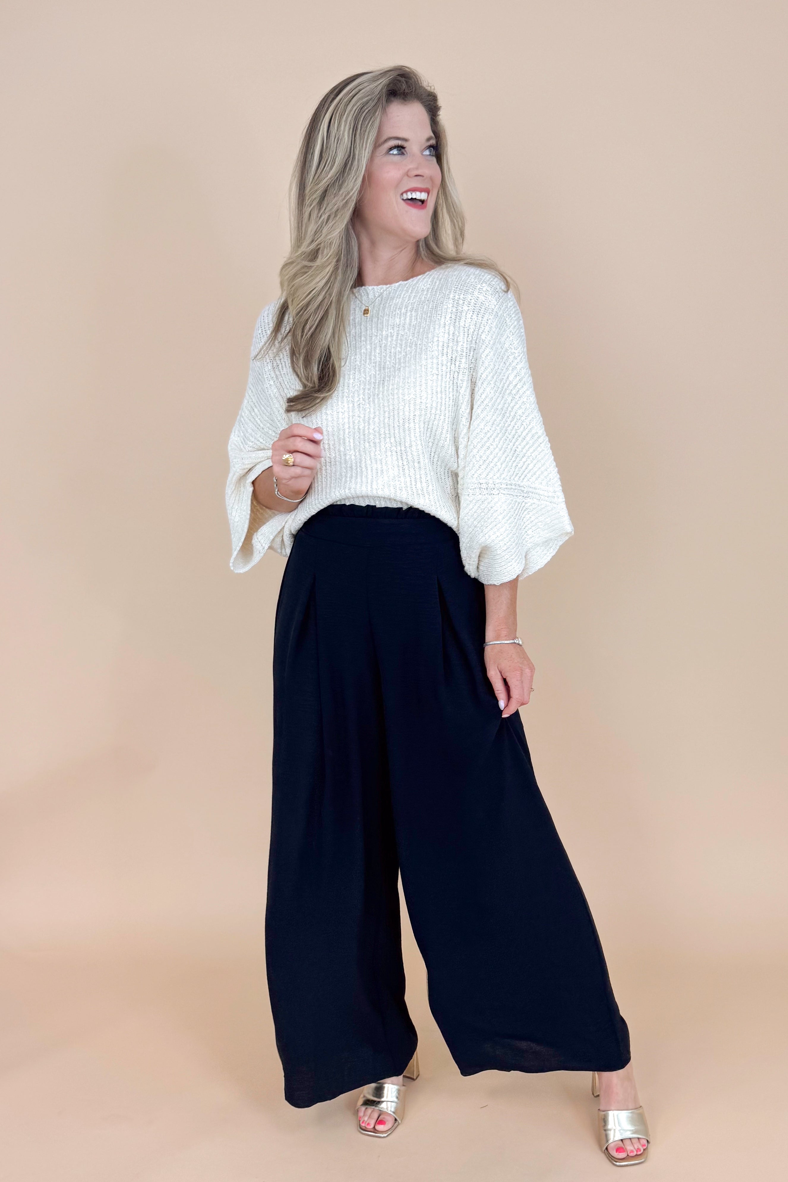 Woman wearing a white blouse and black wide-leg pants against a beige background