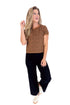 Woman wearing a patterned top and black pants on a white background