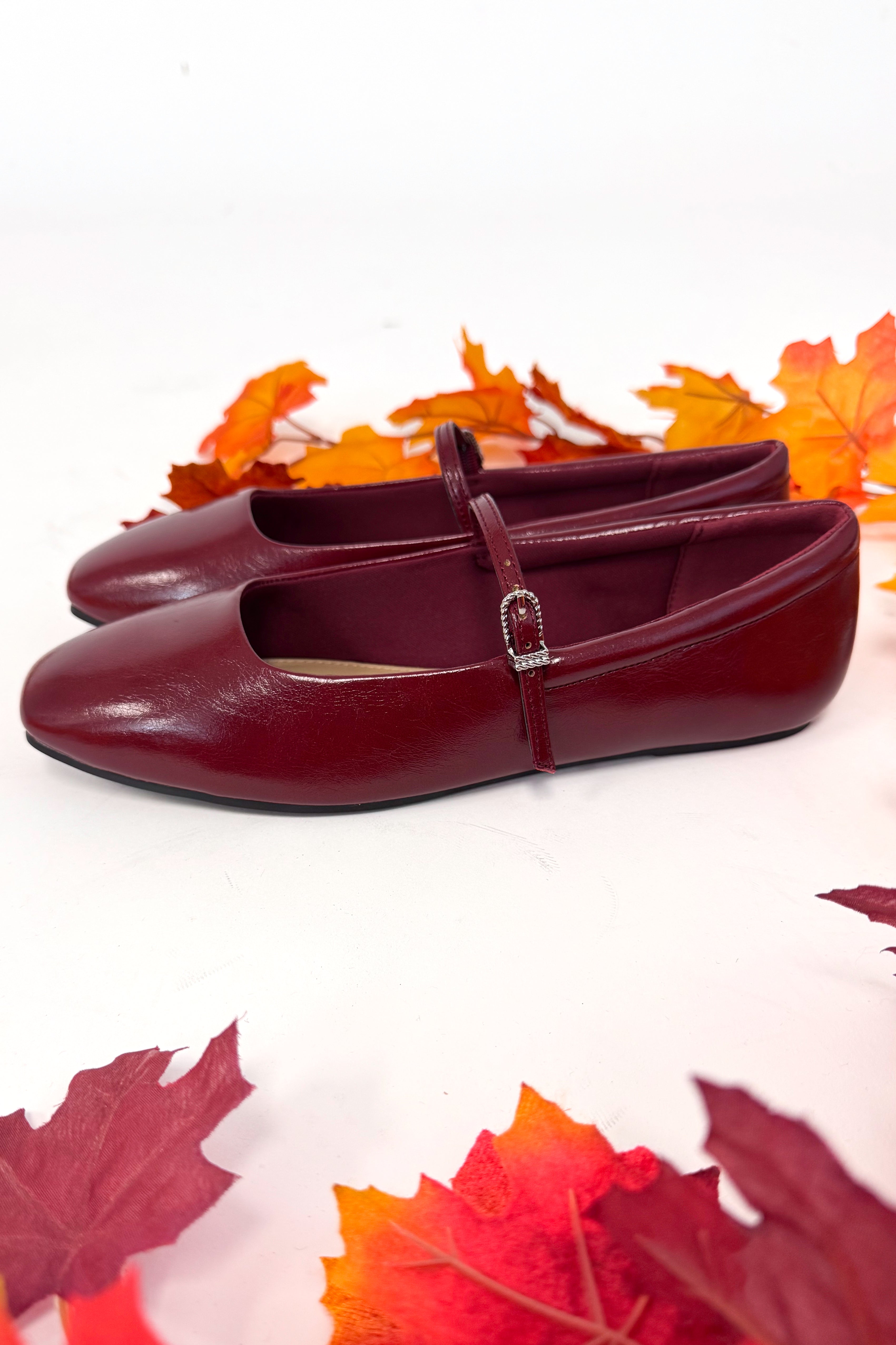 Red shoes with a strap on a white background with autumn leaves.