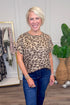 Woman wearing a leopard print top and blue jeans in a clothing store setting.