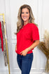 Woman wearing a red shirt and blue jeans standing in a room with white paneled walls and decorative elements.