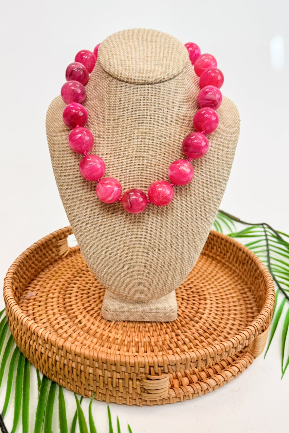 Necklace with pink beads on a beige mannequin bust with a woven base.