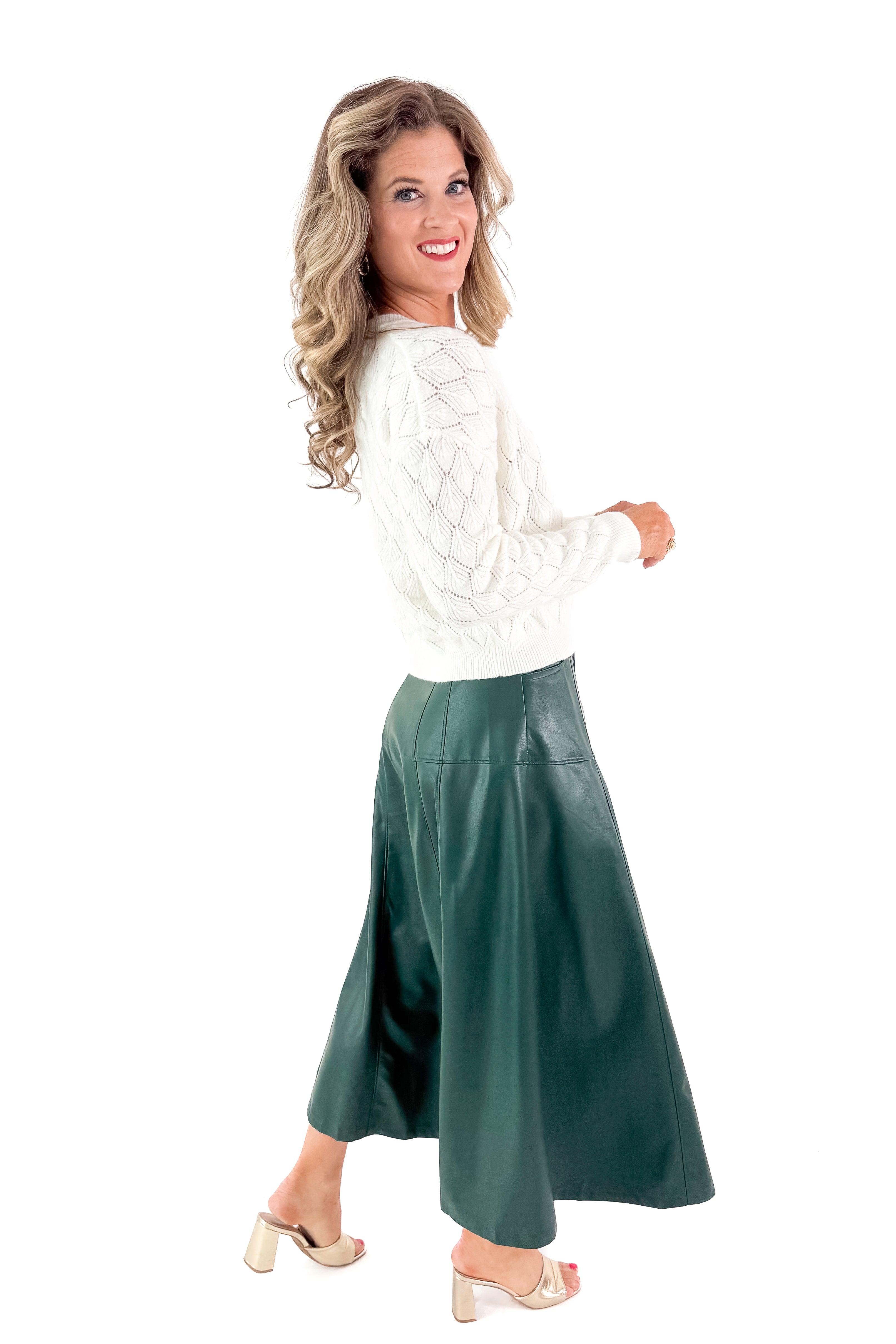 Side view of woman wearing Hunter Green Faux Leather Midi Skirt with top against white studio background.