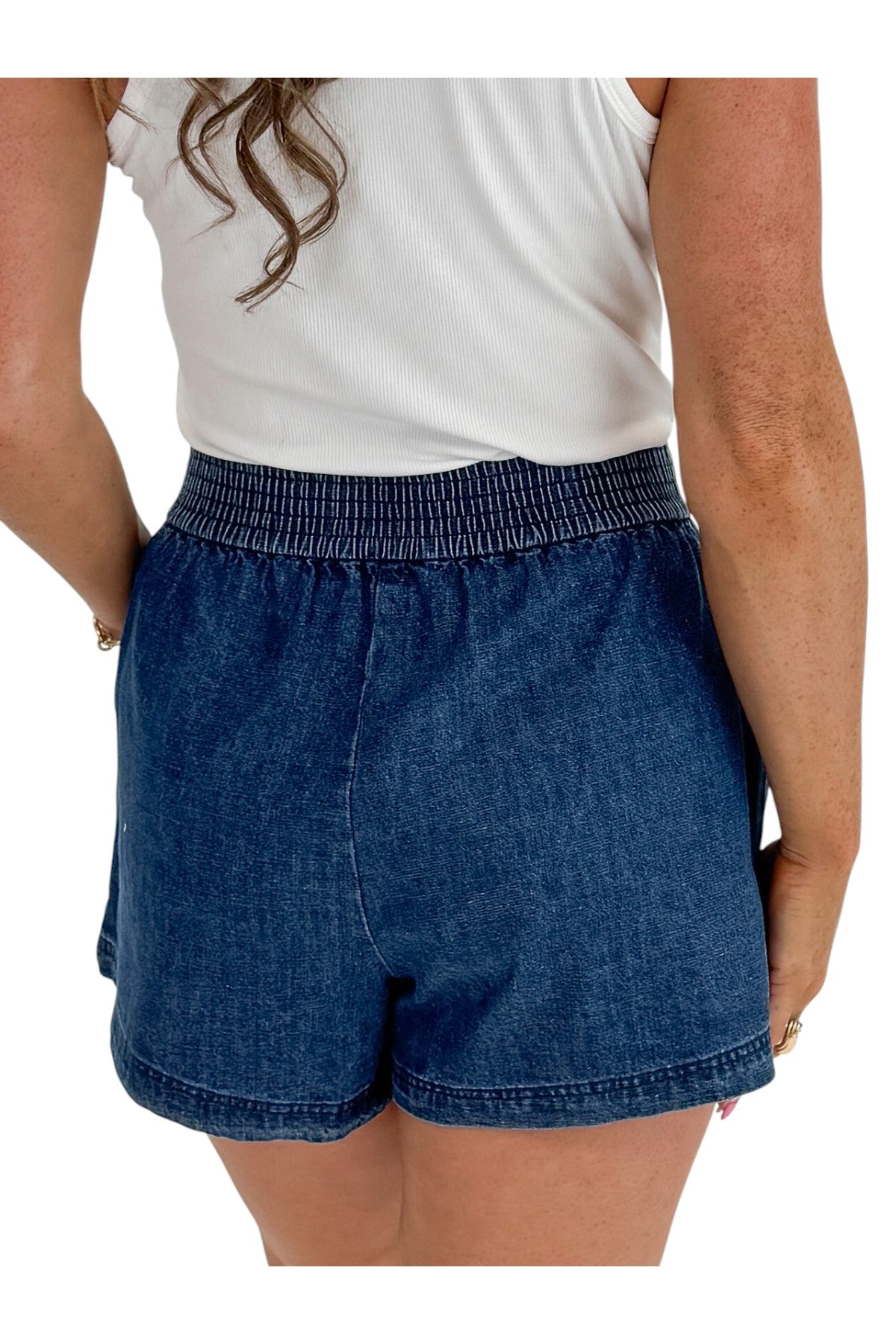 Back detail view of woman wearing Swagger Boutiqueβs Indigo Denim Shorts With Elastic Waist with top against white studio background.