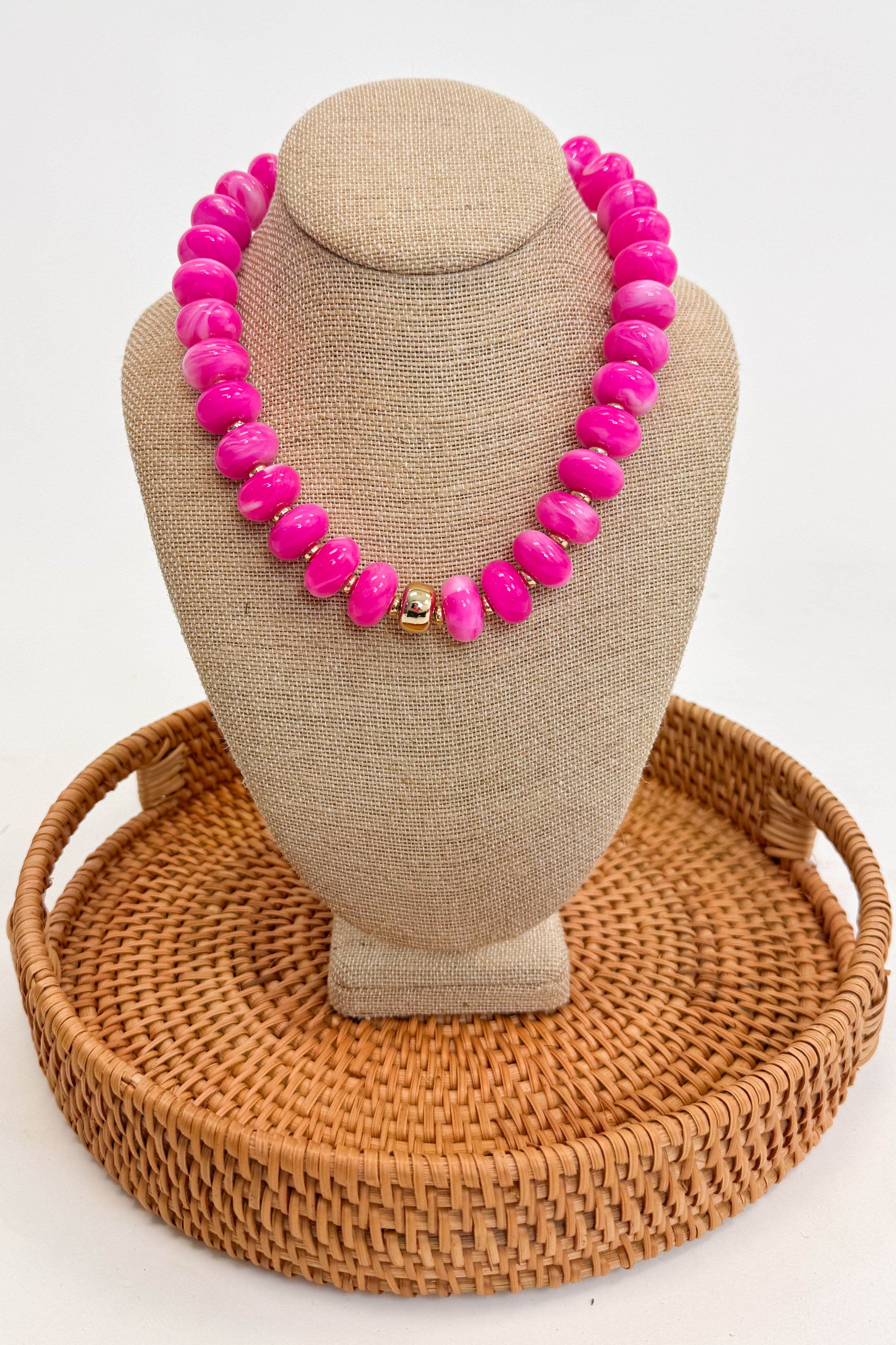 Necklace with pink beads on a beige mannequin bust with a woven brown base.