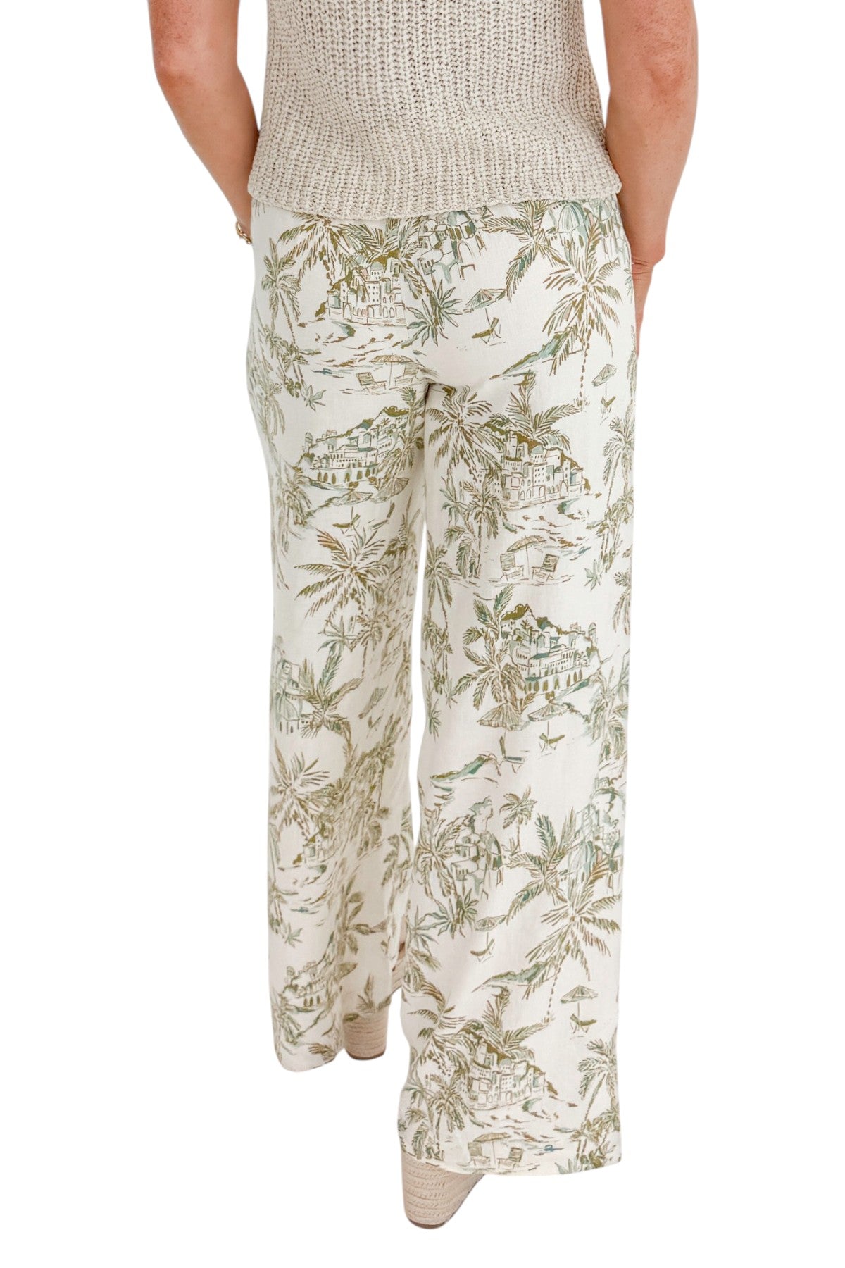 Back view of woman wearing Swagger Boutiqueās Island Coconut Overlook Tiki Tide Linen Pants with Beige V-Neck Knitted Tank by Skies Are Blue against white studio background.