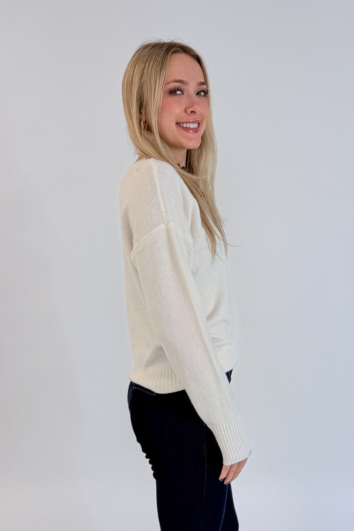 Side view of woman wearing Swagger Boutique’s Ivory Ribbed Hem Sweater with jeans against white studio background.