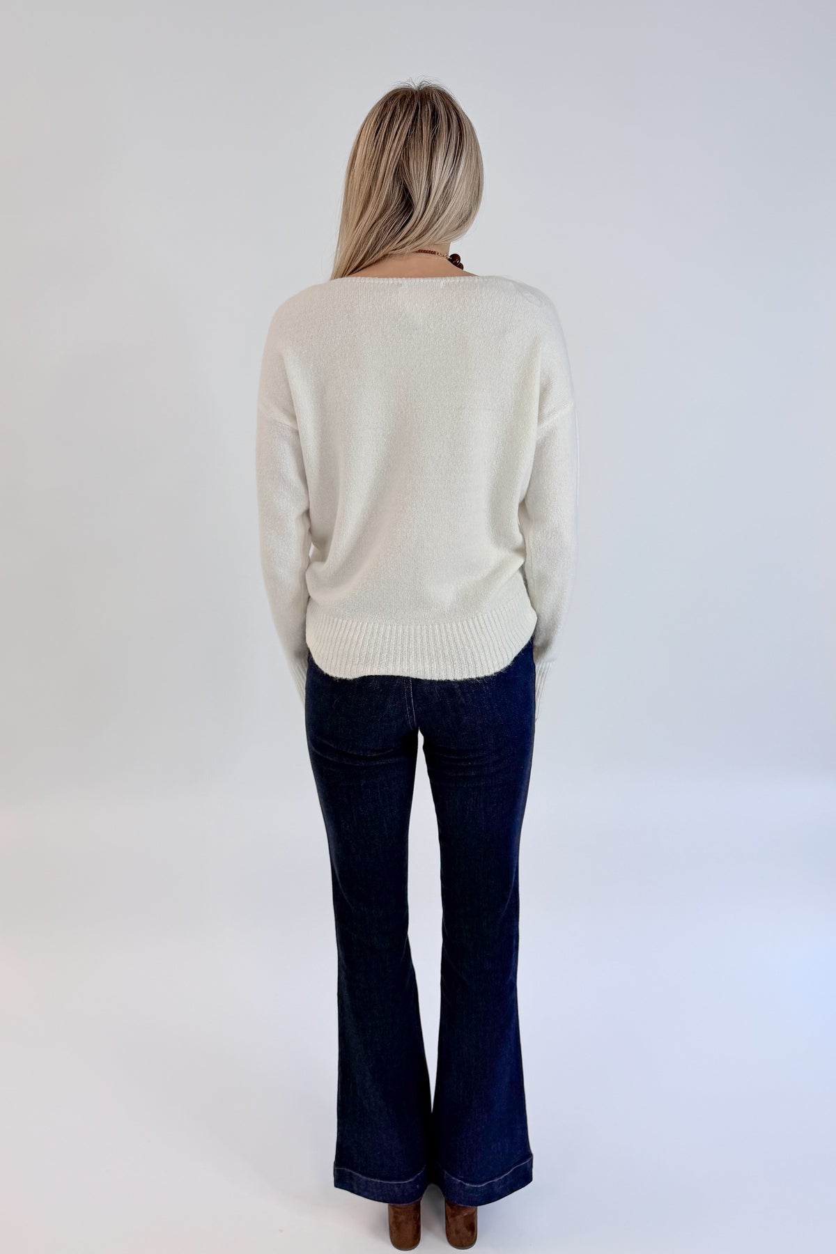 Back view of woman wearing Swagger Boutique’s Ivory Ribbed Hem Sweater with jeans against white studio background.
