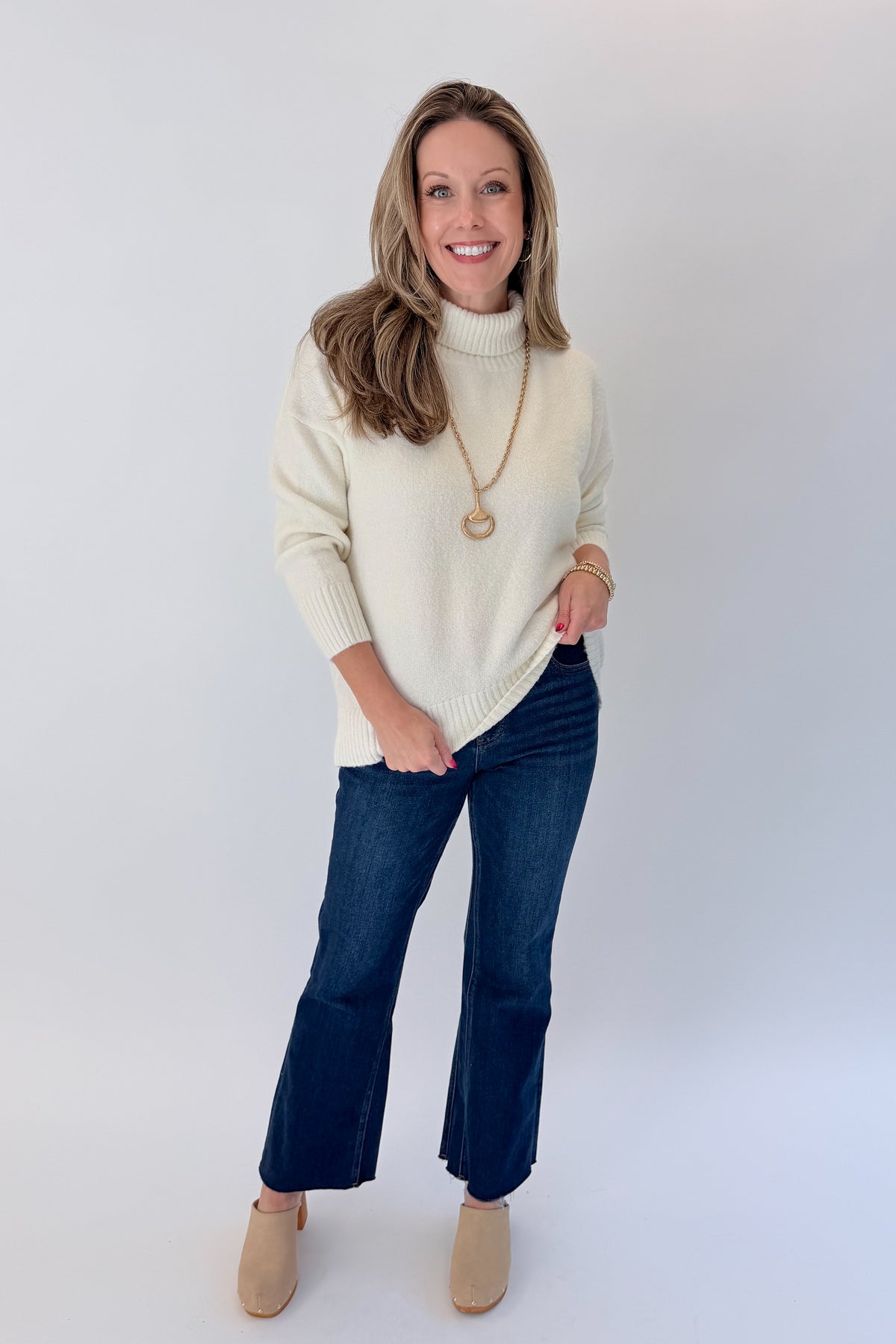 Front view of woman wearing Swagger Boutique’s Ivory Turtleneck Sweater with jeans against white studio background.