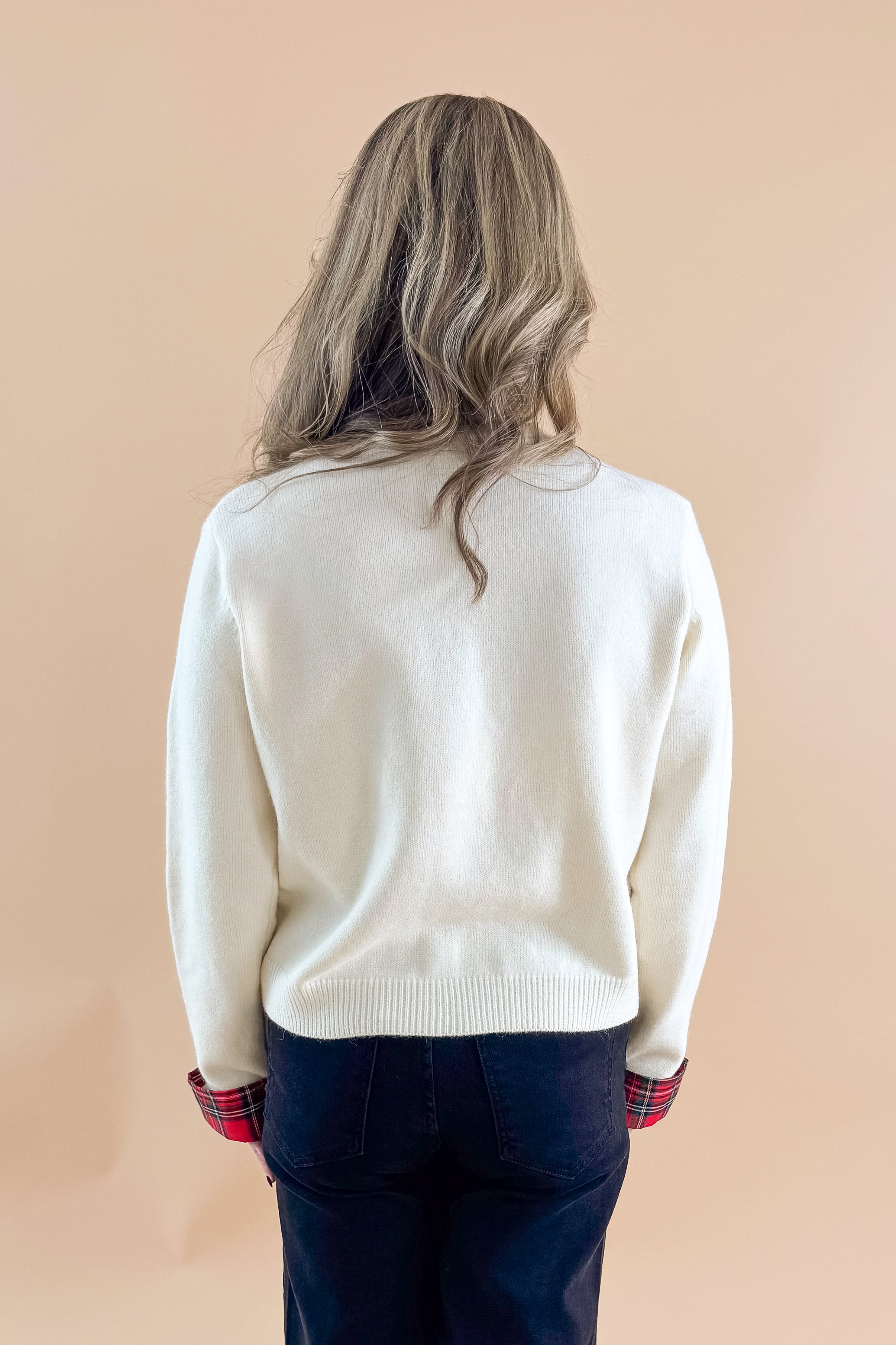 Back view of woman wearing Cream With Tartan Detail Button Up Cardigan with jeans against tan studio background.