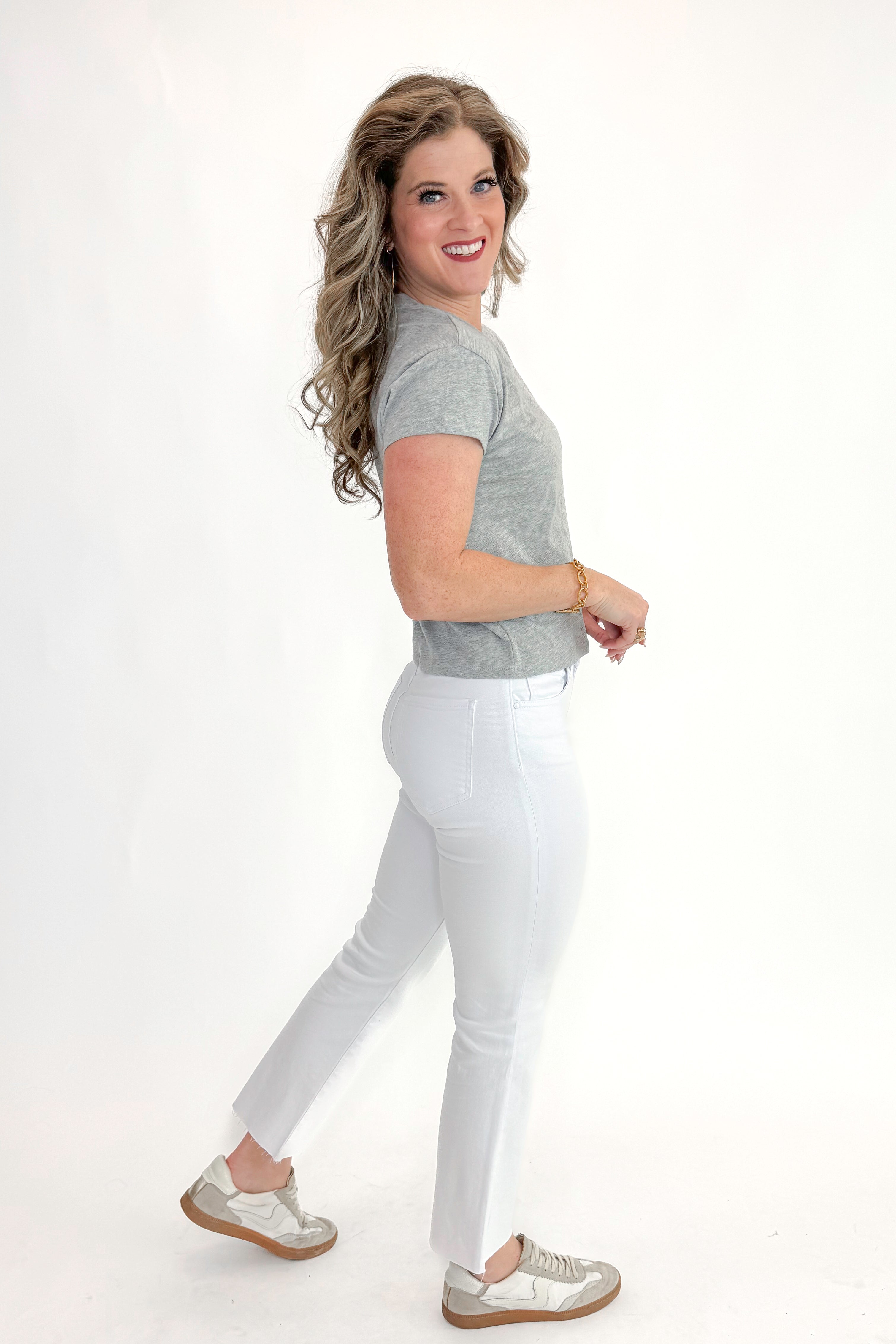 Side view of woman wearing top with Kelsey Optic White Ankle Flare Jeans by Kut from the Kloth against white studio background.