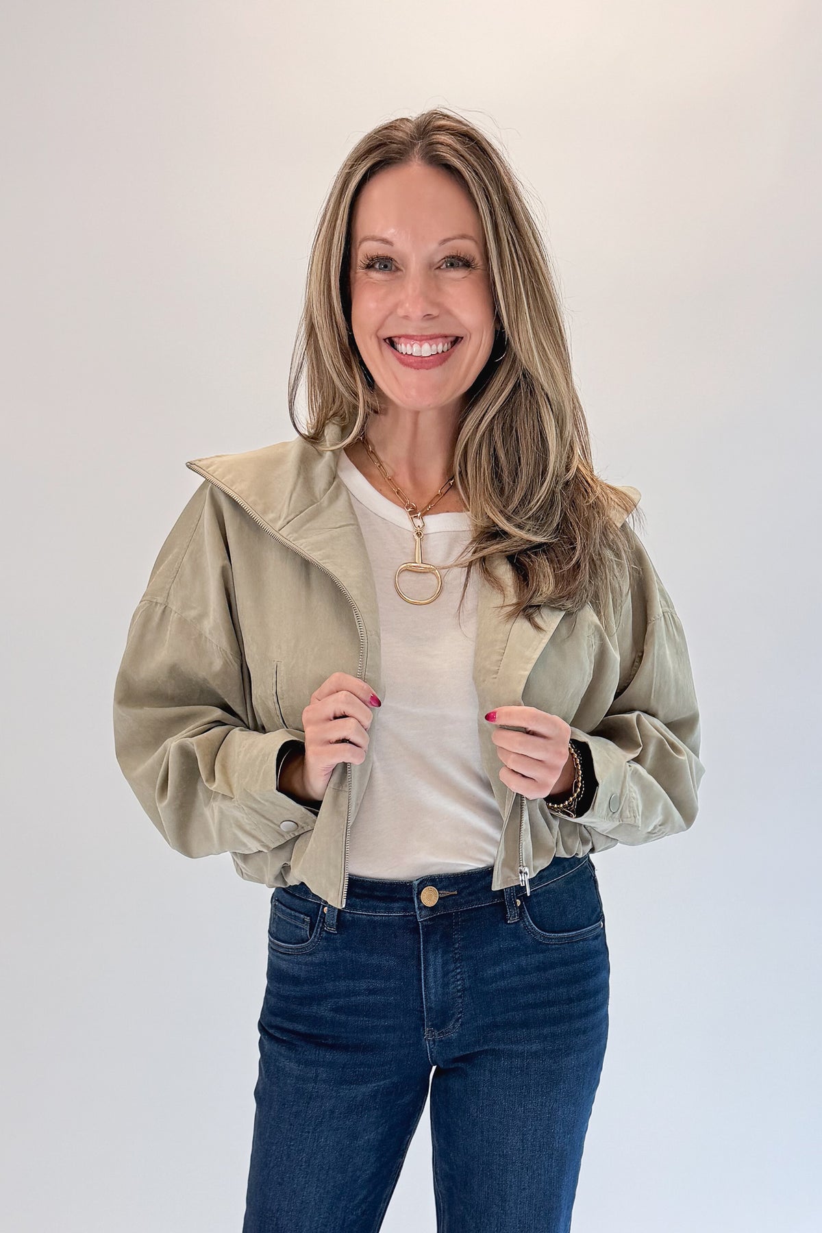 Front view of woman wearing Swagger Boutique’s Khaki Bubble Hem Bomber Jacket with jeans against white studio background.