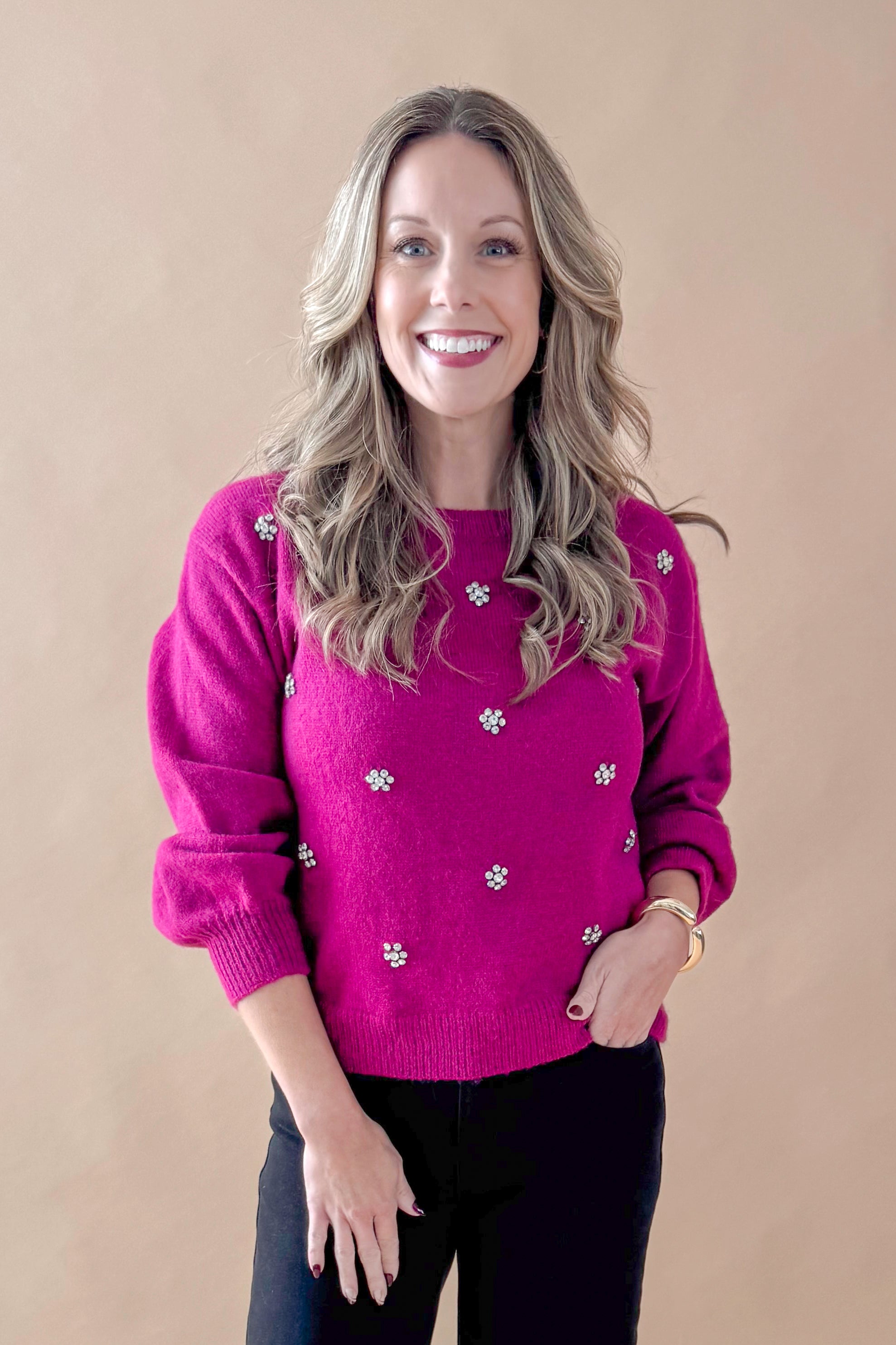 Front view of woman wearing Magenta Rhinestone Detail Sweater with jeans against tan studio background.
