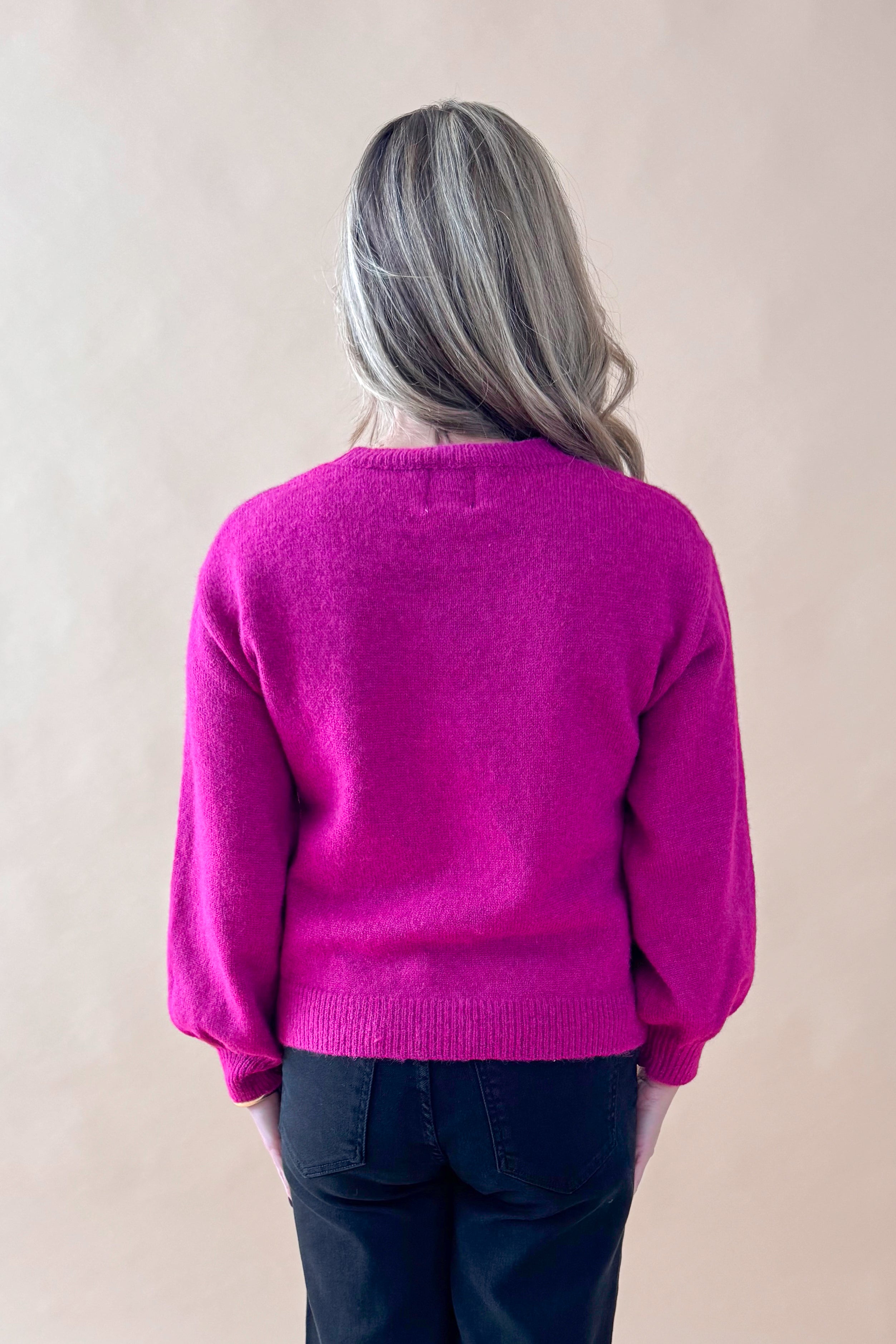 Back view of woman wearing Magenta Rhinestone Detail Sweater with jeans against tan studio background.