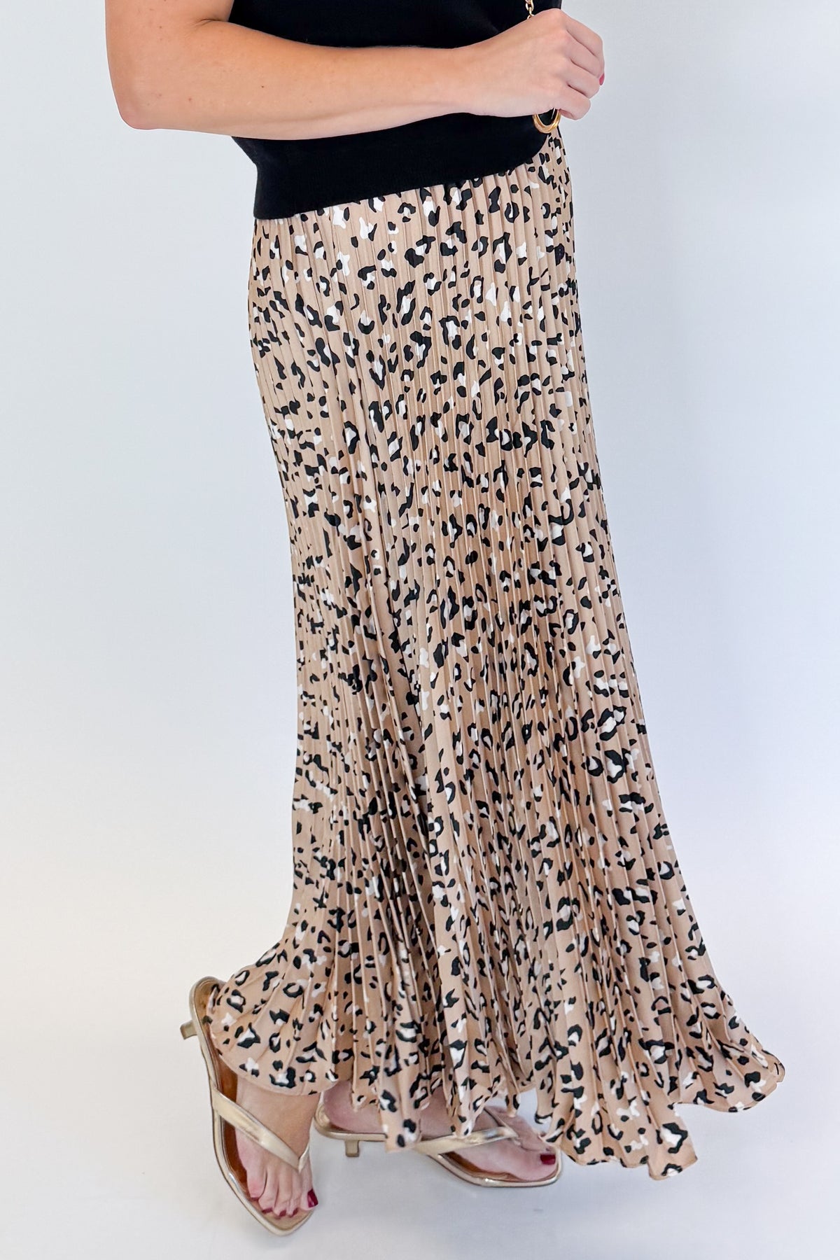 Side detail view of woman wearing Swagger Boutique’s Leopard Pleated Skirt & Black Short Sleeve Twist Detail Sweater against white studio background.