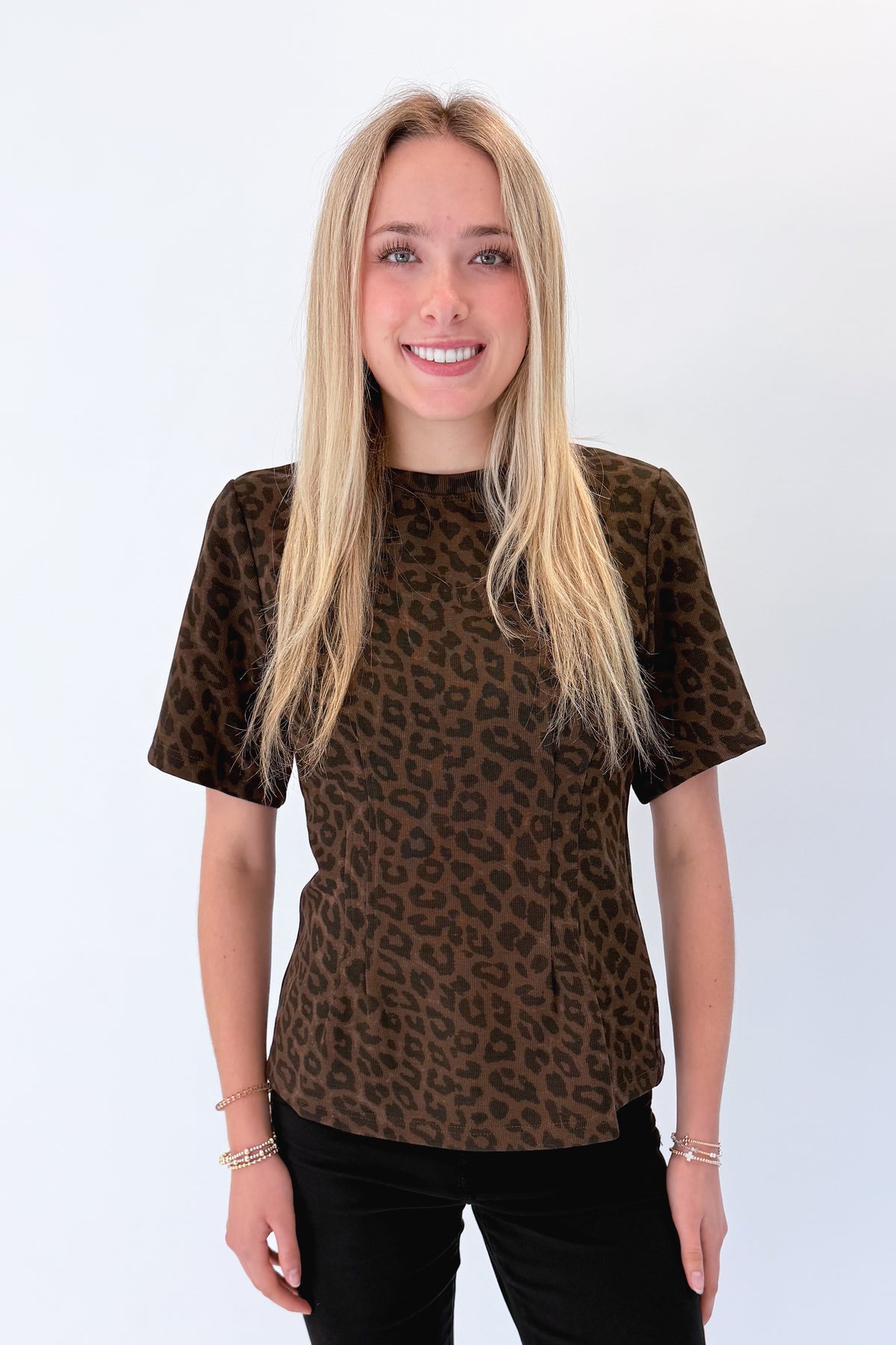 Front view of woman wearing Swagger Boutique’s Leopard Pleated Top with jeans against white studio background.