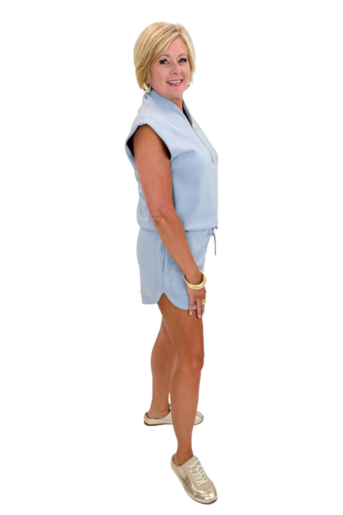 Side view of woman wearing Swagger Boutiqueās Light Blue Sleeveless 1/4 Zip Top with matching shorts against white studio background.