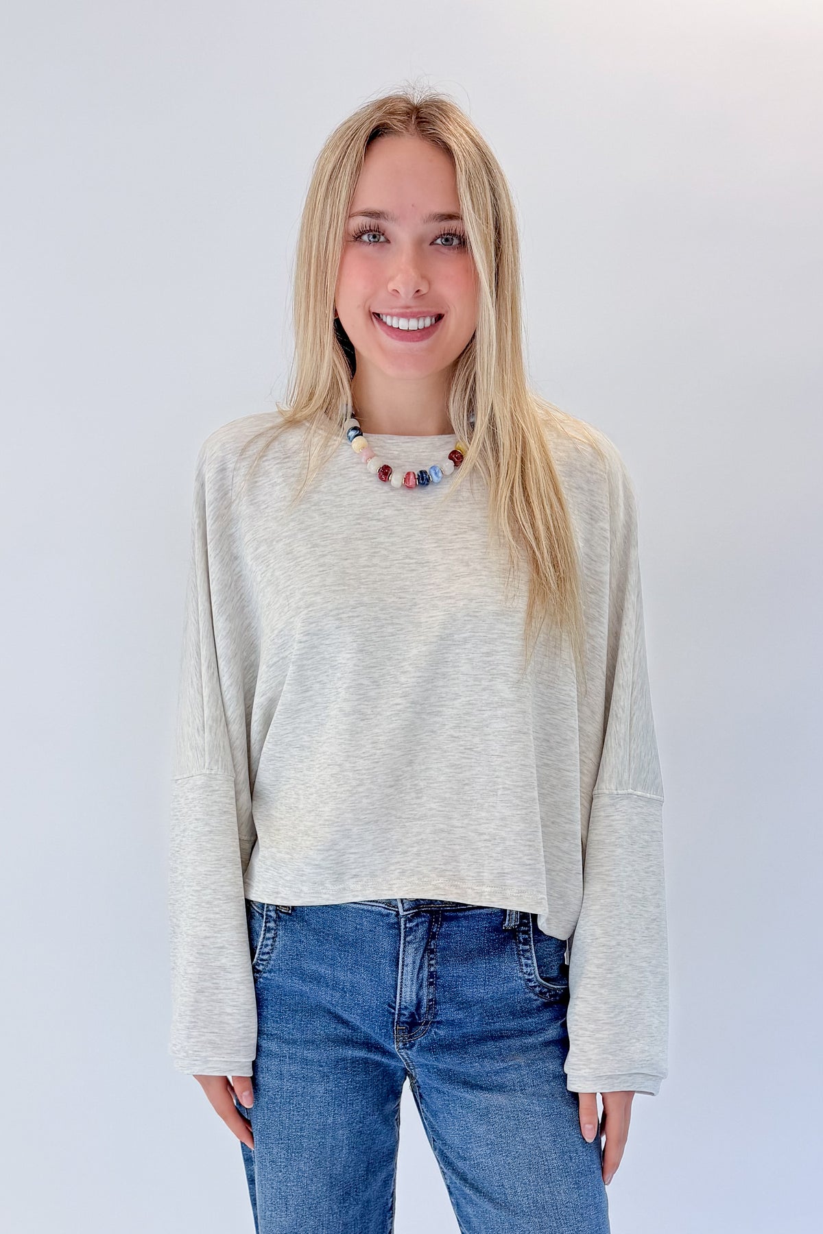 Front view of woman wearing Swagger Boutique’s Light Grey Cropped Sweatshirt with jeans against white studio background.