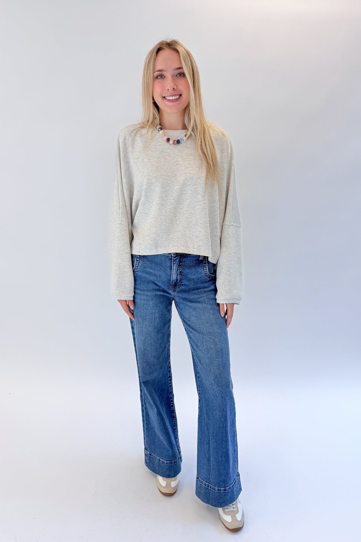 Front view of woman wearing Swagger Boutique’s Light Grey Cropped Sweatshirt with jeans against white studio background.