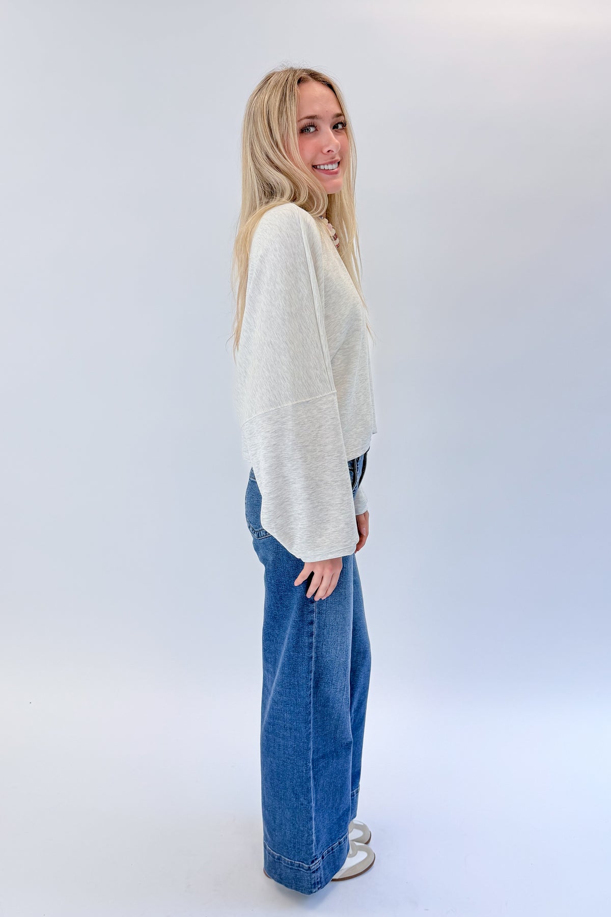 Side view of woman wearing Swagger Boutique’s Light Grey Cropped Sweatshirt with jeans against white studio background.