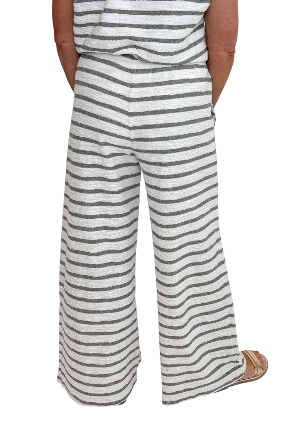 Back detail view of woman wearing Swagger Boutiqueβs Light Grey Striped Short Sleeve Top with matching Light Grey Striped Lounge Pants against white studio background.