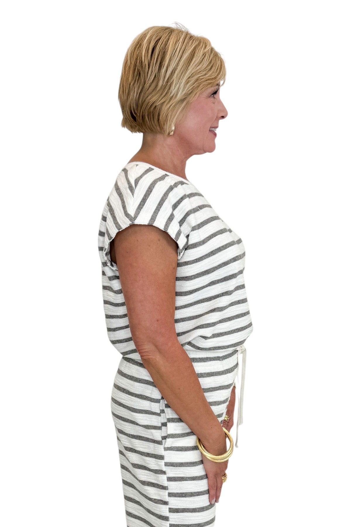 Side view of woman wearing Swagger Boutiqueβs Light Grey Striped Short Sleeve Top with matching Light Grey Striped Lounge Pants against white studio background.