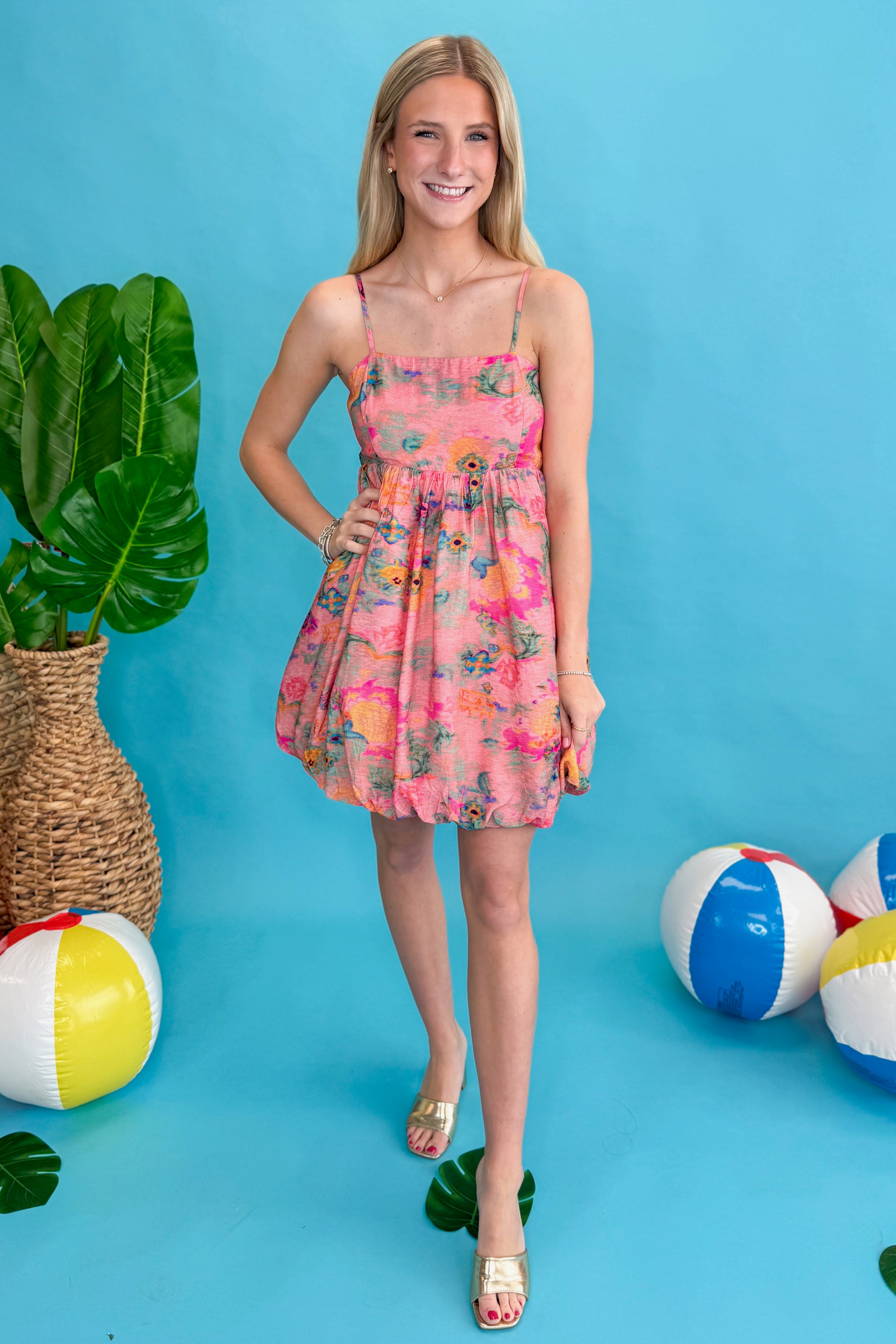 Front view of woman wearing Pink & Multi Printed Bubble Hem Tank Dress against blue beachy background.